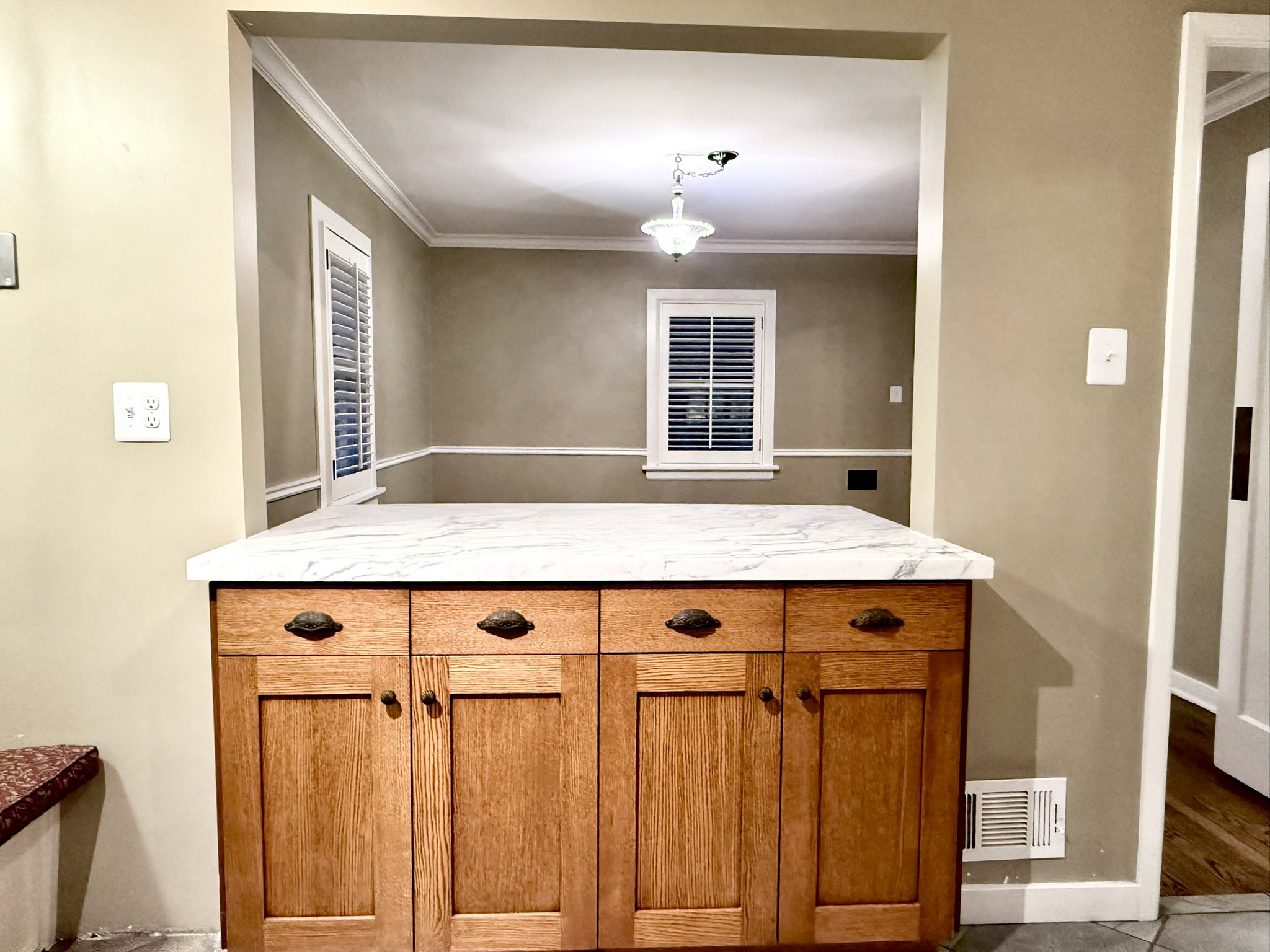 Wood-finish cabinetry with a white marble-look countertop, featuring a pass-through opening to an adjacent room