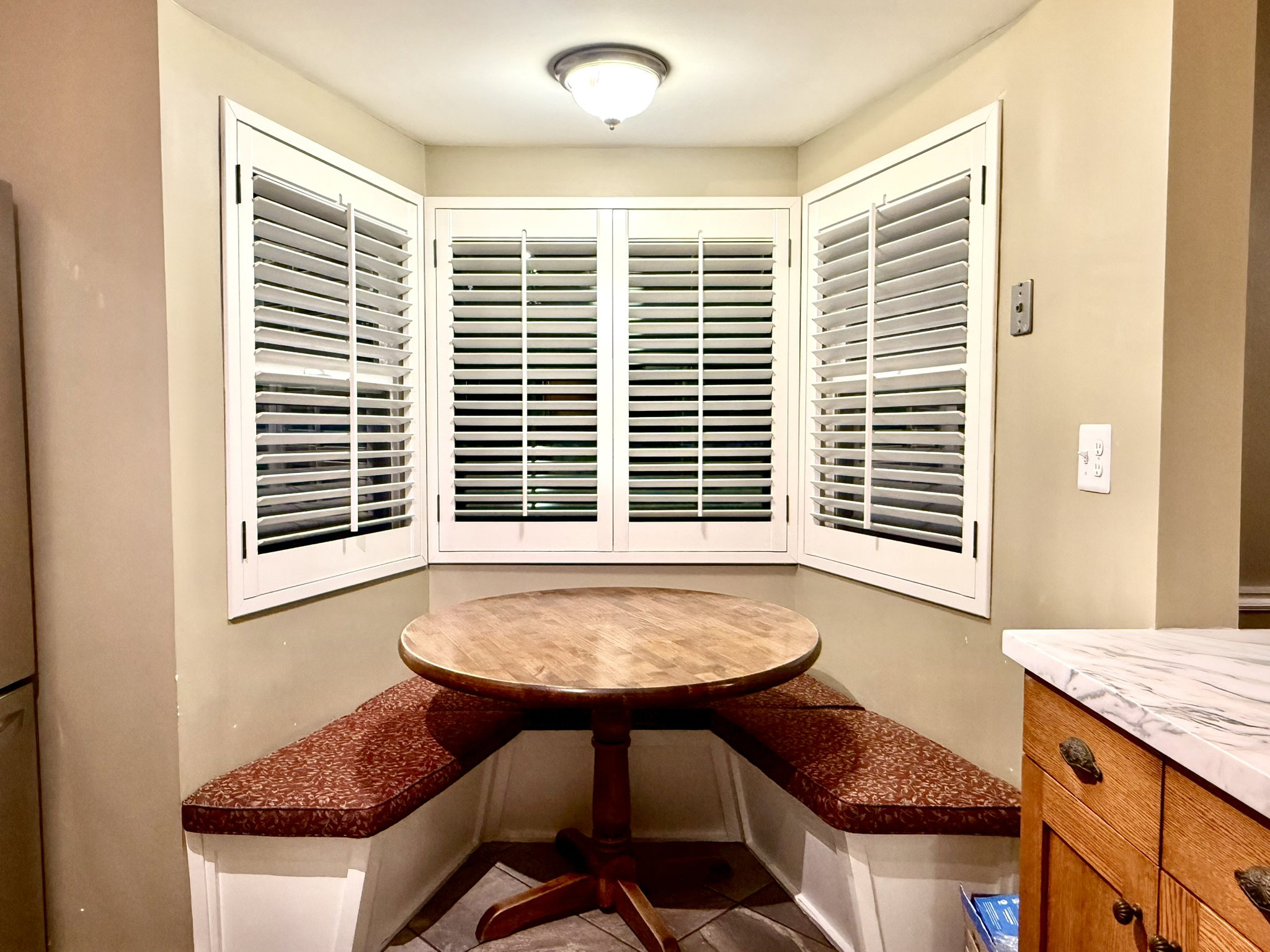 Built-in corner bench seating with patterned cushions, complemented by bay windows featuring white plantation shutters