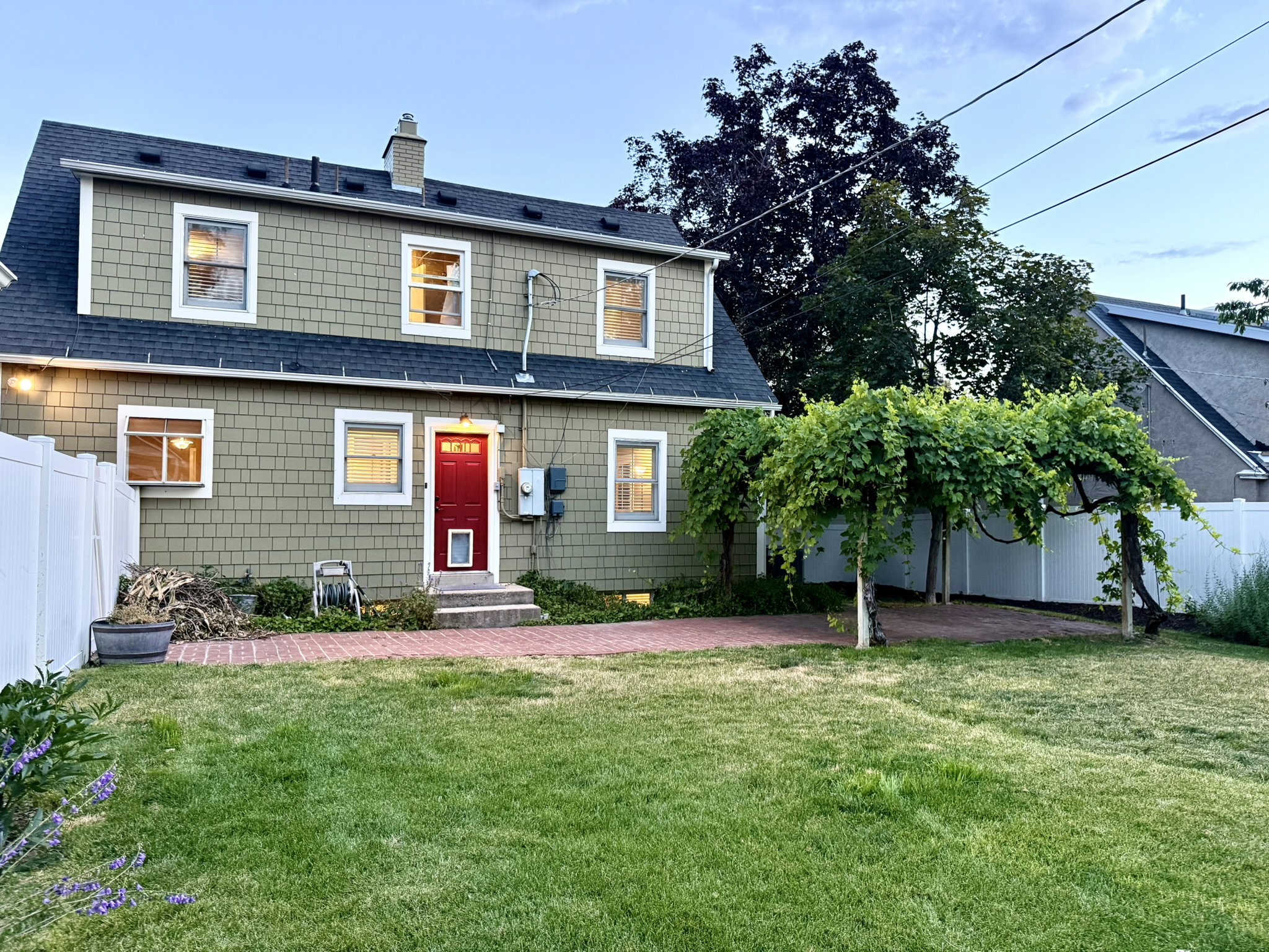 Expansive backyard featuring a manicured lawn, brick patio, and mature vine-covered arbor