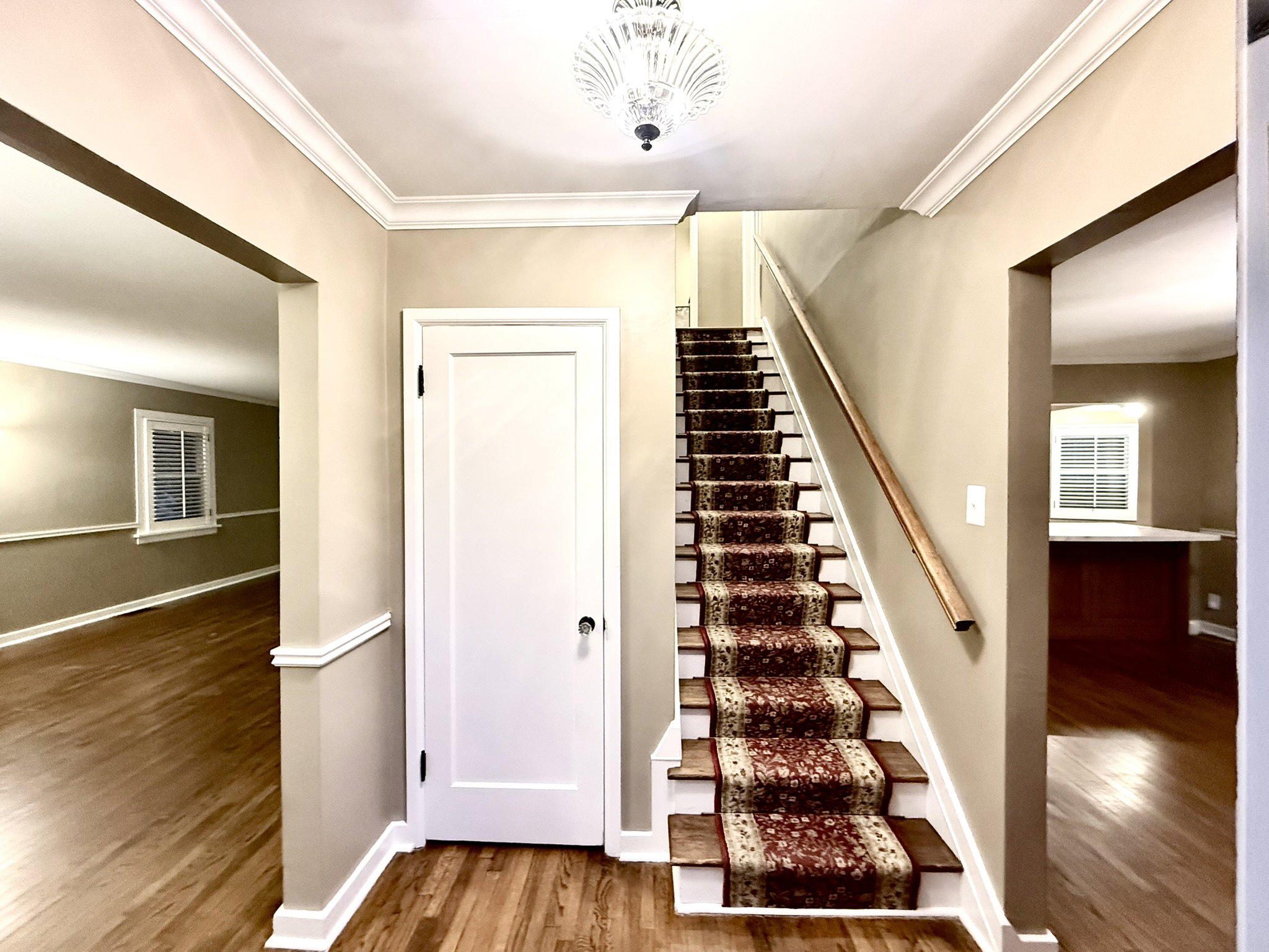 Foyer featuring wood-finish flooring, a carpeted staircase with wood handrail, and crown molding