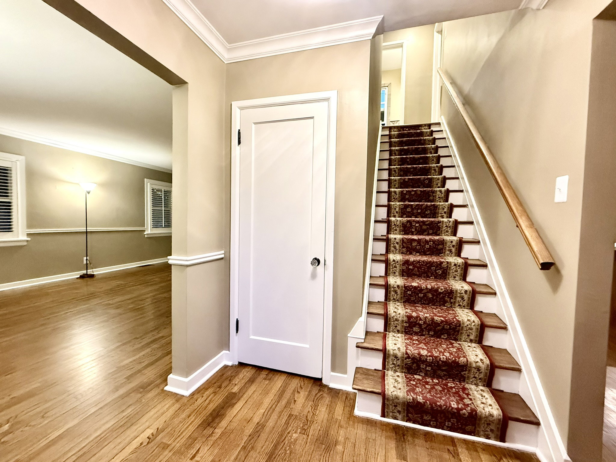 Entryway featuring wood-finish flooring, a carpeted staircase with a wooden handrail, and an arched doorway leading to an additional space