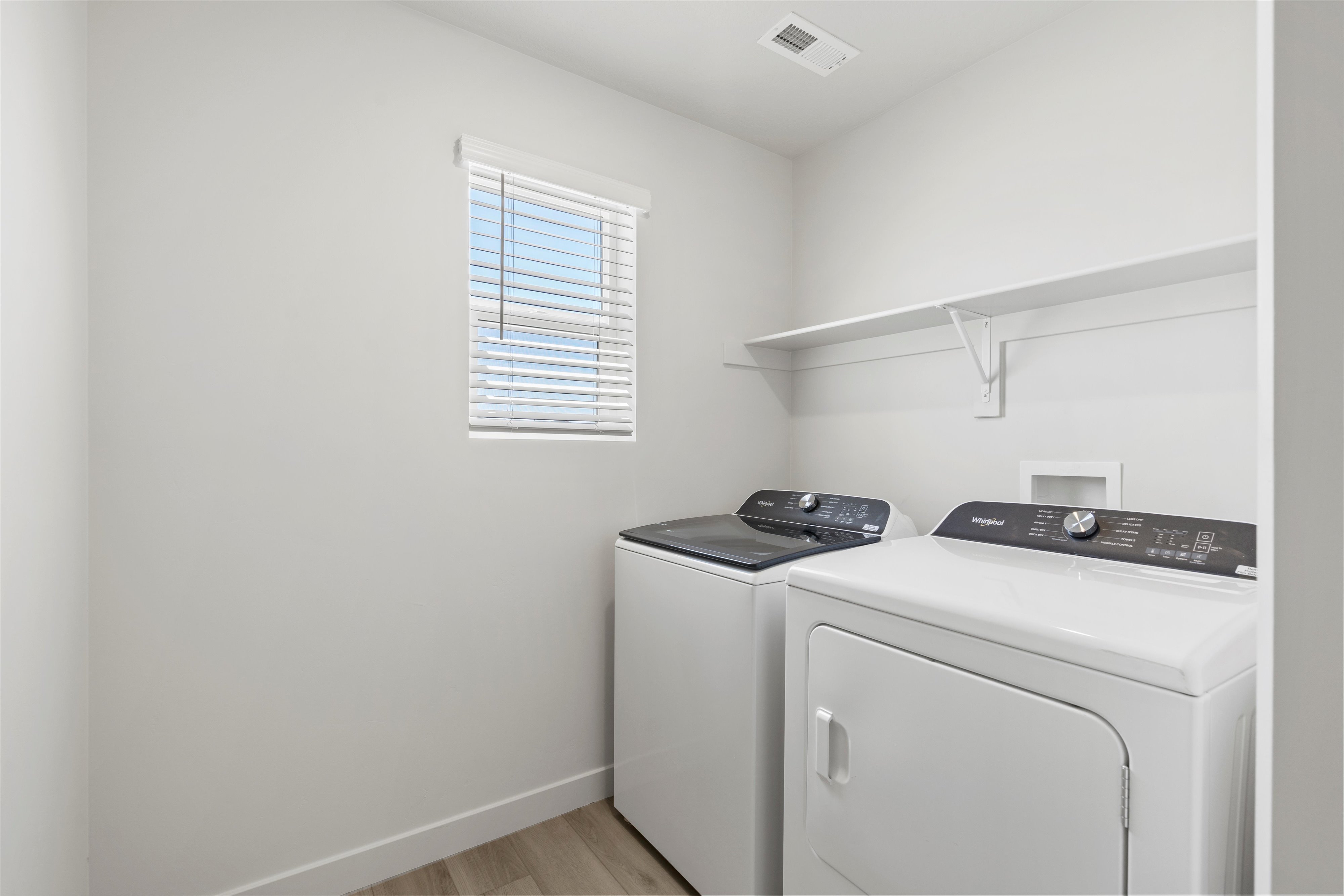 **DISCLAIMER** Interior package may vary. Dedicated laundry area featuring a window with blinds, upper shelving, light wood-finish flooring, and white walls