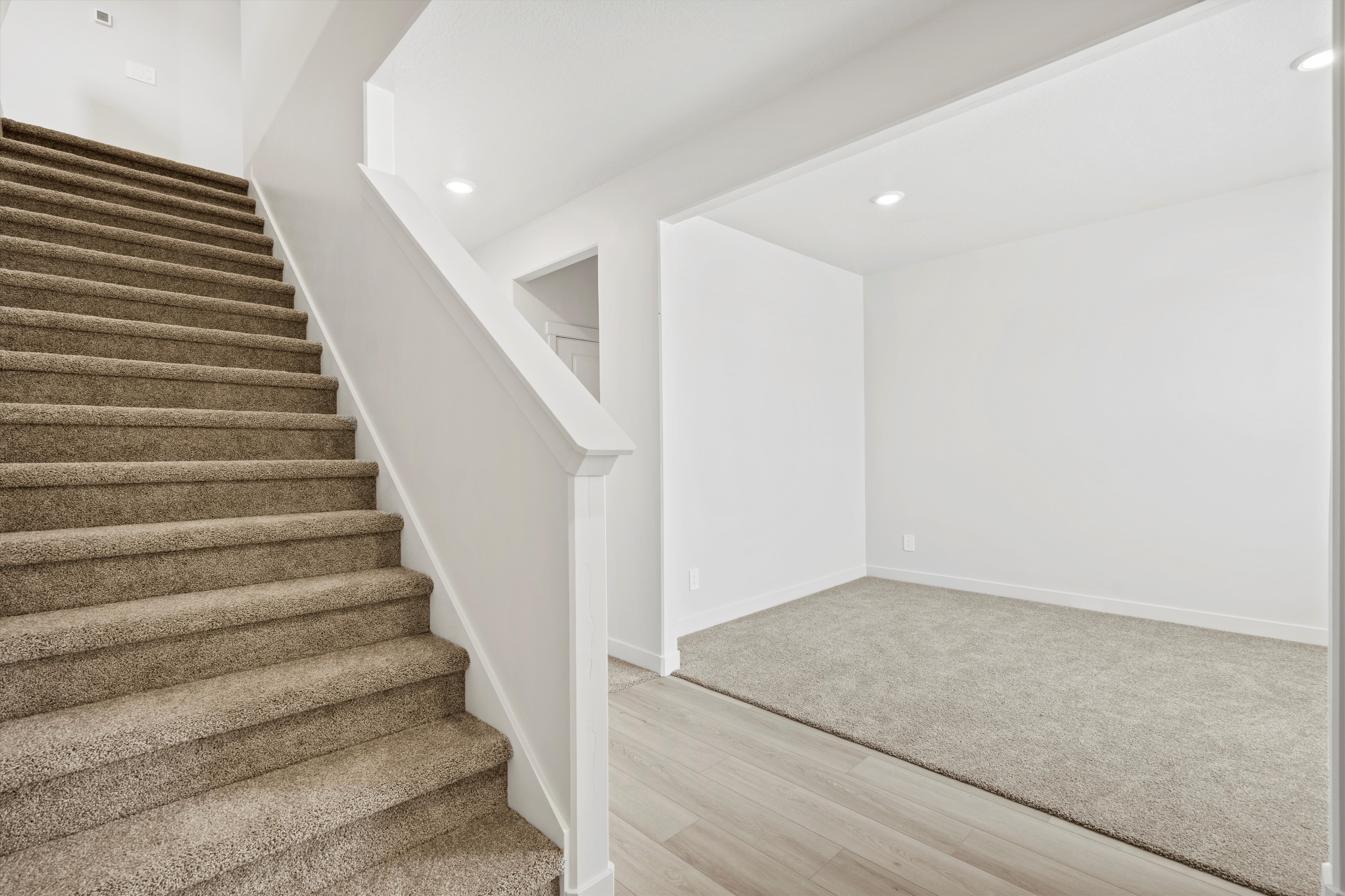**DISCLAIMER** Interior package may vary. Carpeted staircase with white balustrade, recessed lighting, and wood-finish flooring extending into an adjacent carpeted room