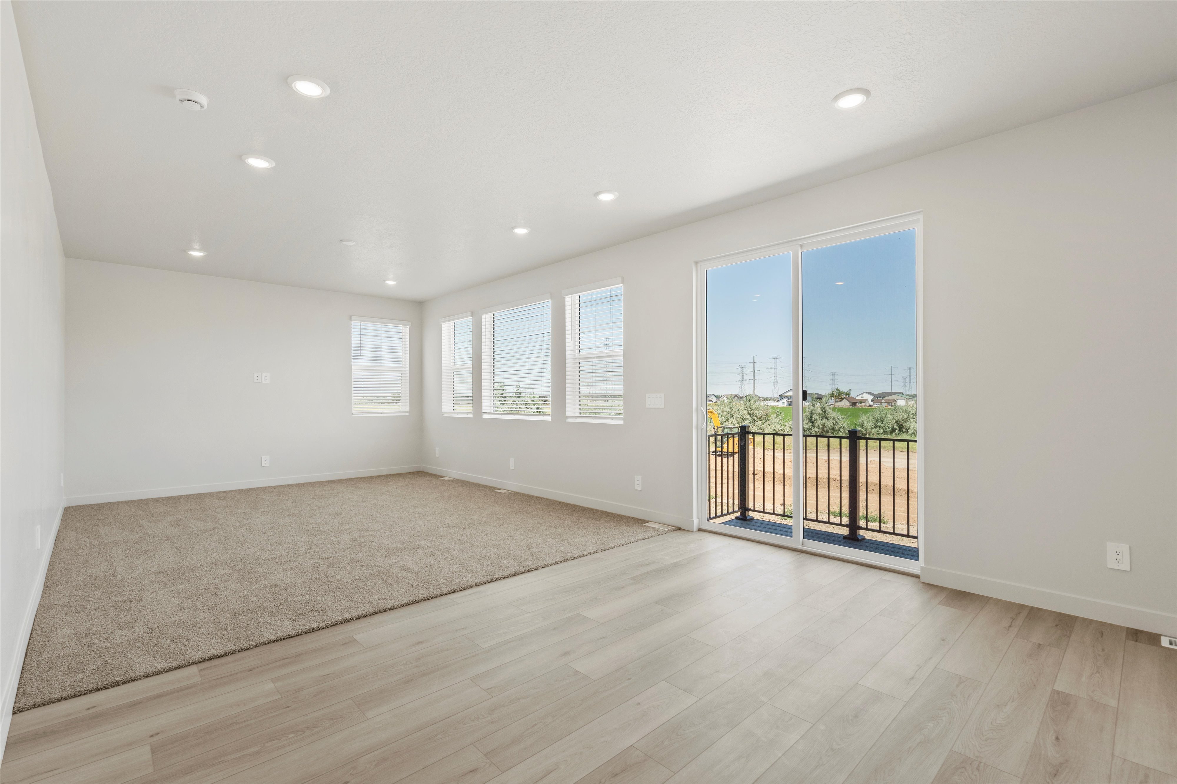 **DISCLAIMER** Interior package may vary. Open-concept room featuring light wood-finish flooring, recessed lighting, and a sliding glass door leading to a balcony with black railings
