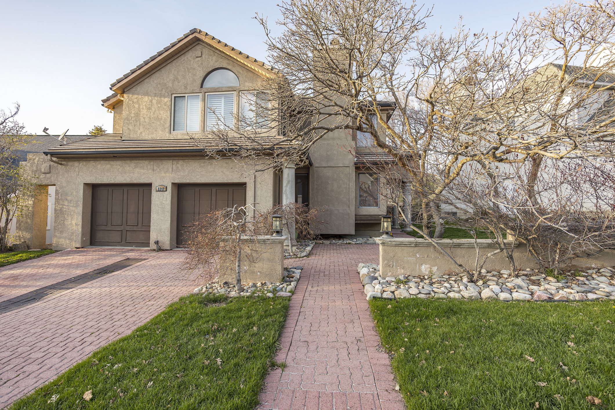 Stucco exterior with a two-car garage, arched window, and red paver driveway