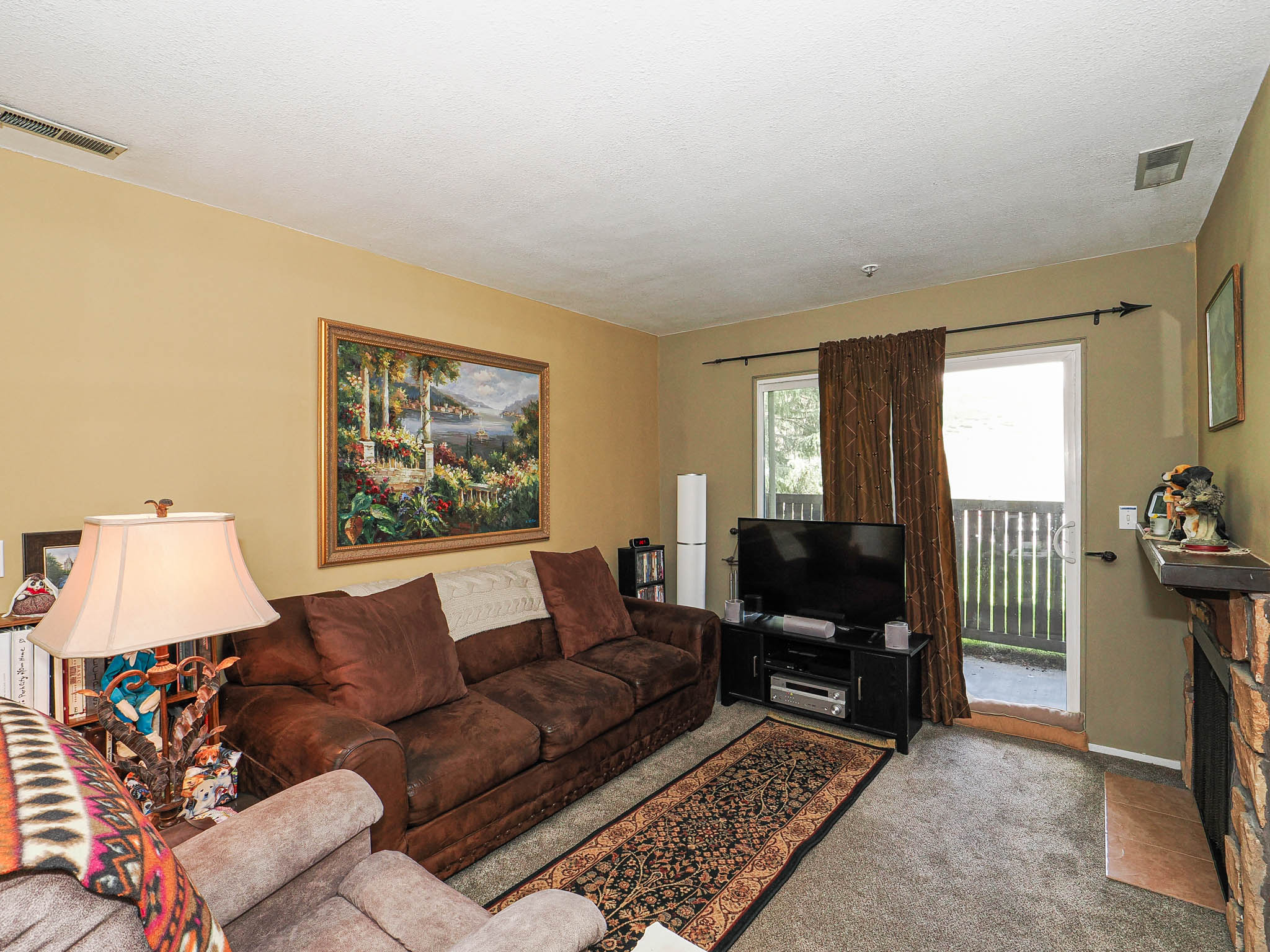 Living area featuring a sliding glass door to an outdoor balcony, a stone-clad fireplace with a wood mantel, a ceiling-mounted air vent, and neutral-toned wall paint