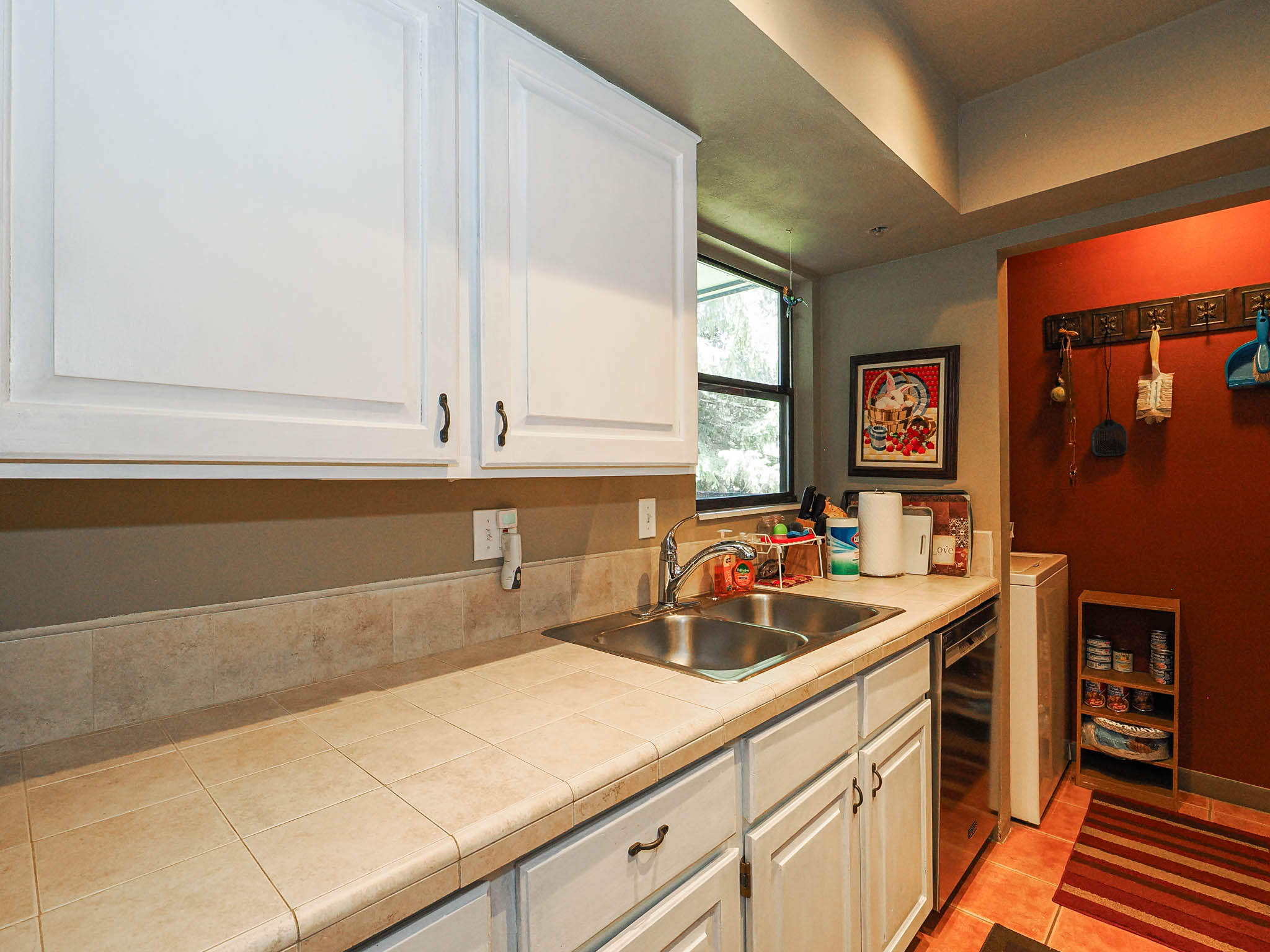 Kitchen featuring white cabinetry with dark hardware, a stainless steel double-basin sink, and a tiled countertop with a matching backsplash