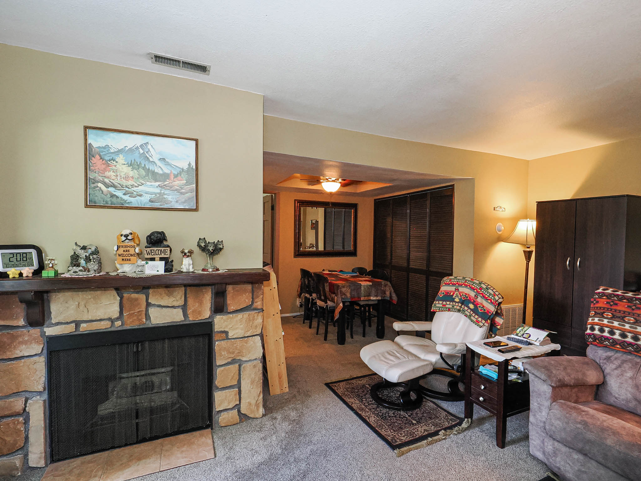 Stone-clad fireplace featuring a wood mantelpiece and a metal screen, complemented by light-toned wall paint and carpeting
