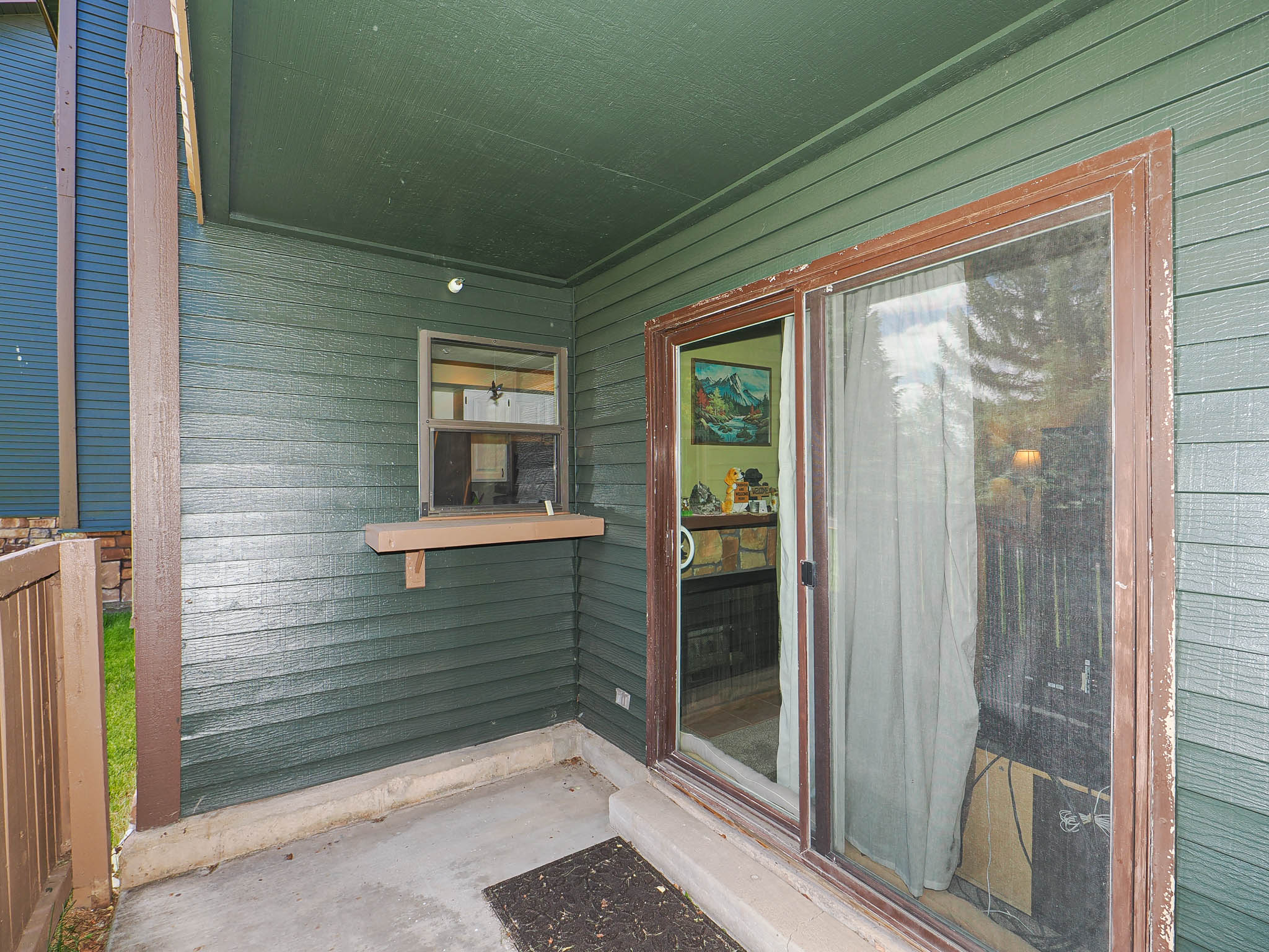 Covered patio with concrete flooring, green horizontal siding, and a wooden sliding glass door