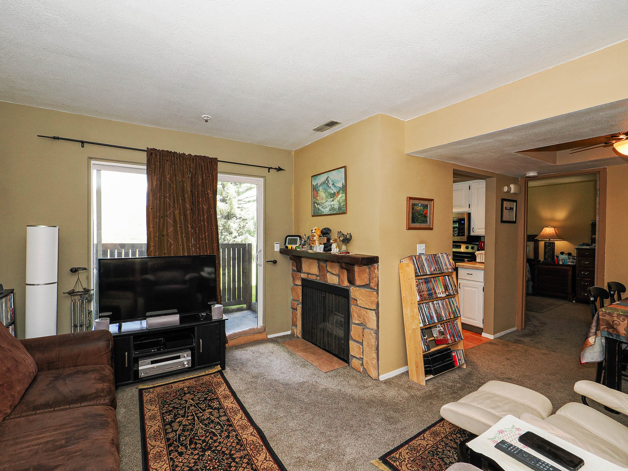 Living area featuring a stone-faced fireplace with a wood mantle, carpet flooring, and a sliding glass door to an exterior space