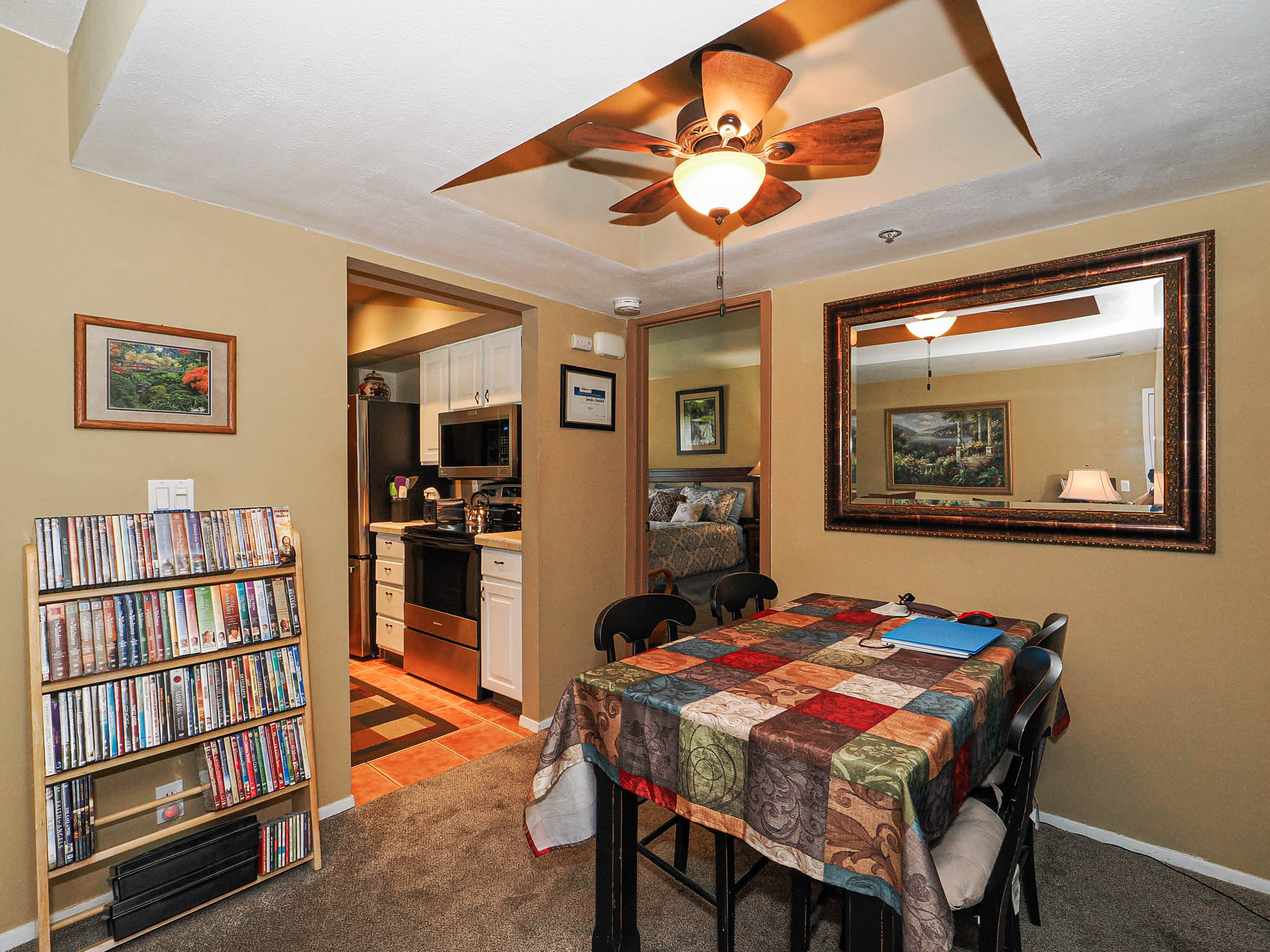 Dining area featuring a decorative ceiling fan, a large framed mirror, and access to an adjacent kitchen with stainless steel appliances