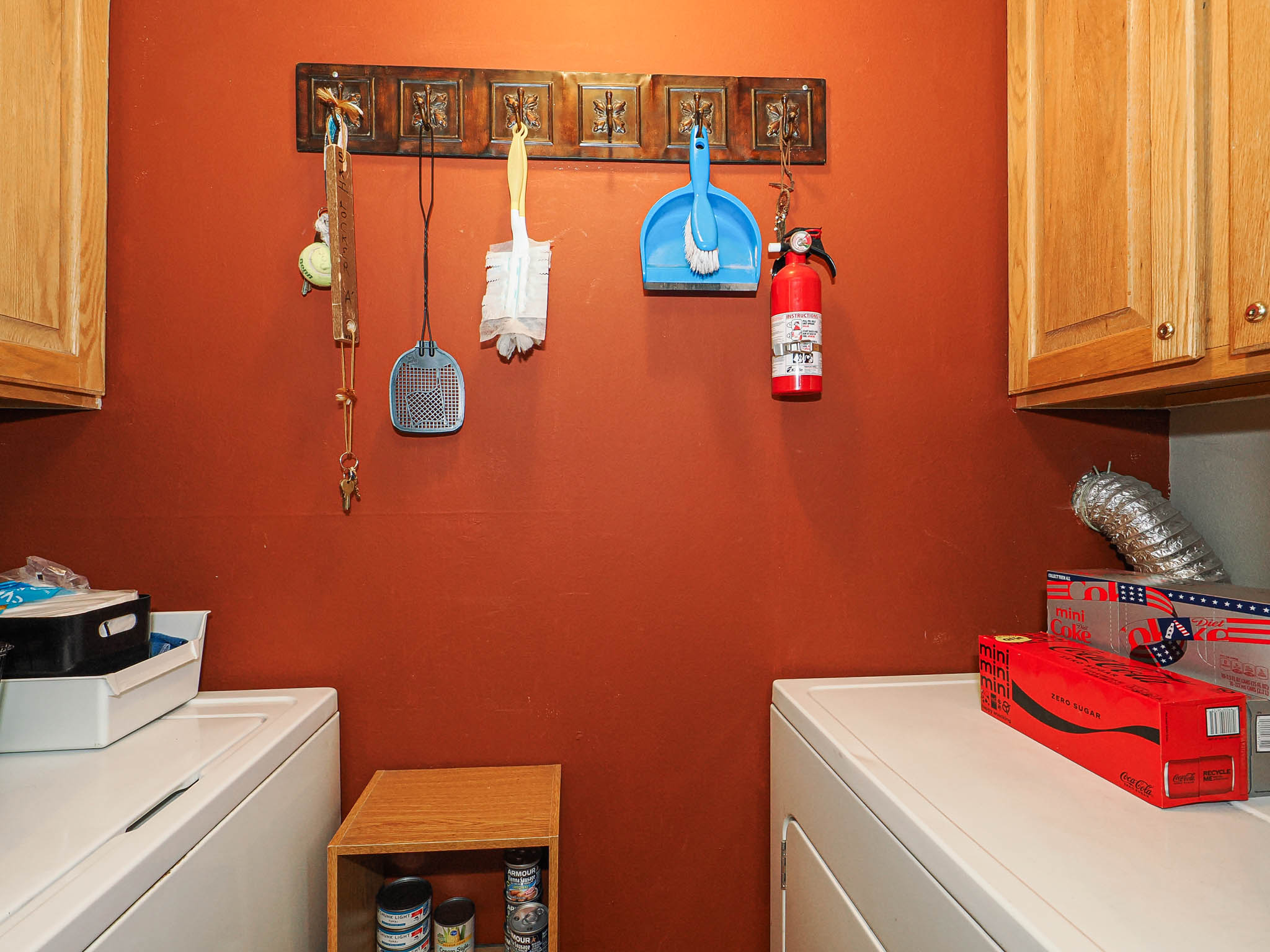 Laundry area featuring wood-finish cabinetry and a hook rack on a rust-toned wall