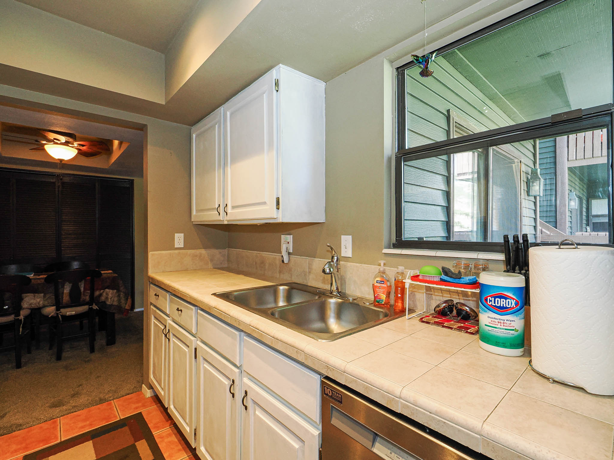 Kitchen workspace featuring a double basin stainless steel sink, white cabinetry, tile countertops, and a tile backsplash