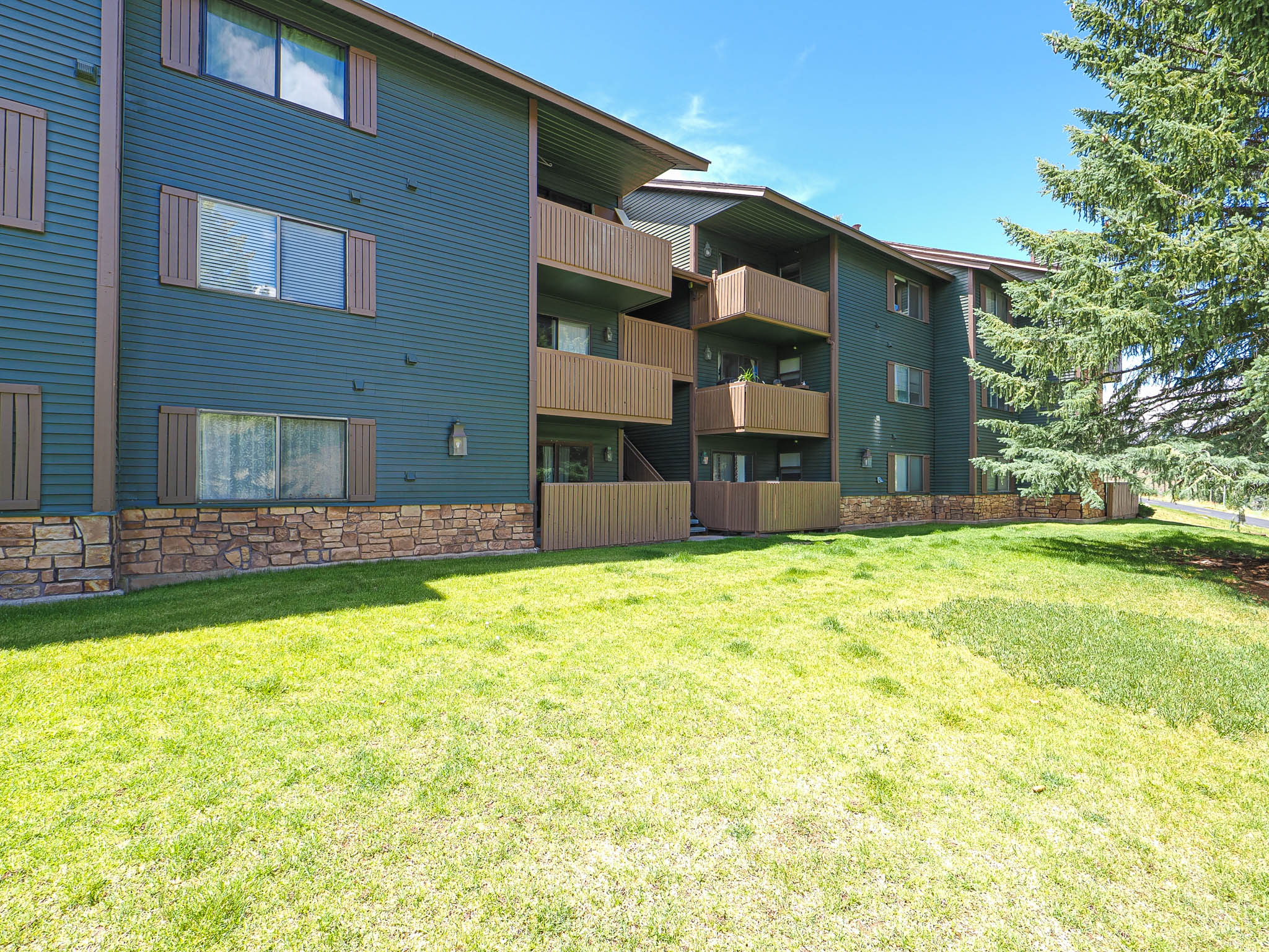 Multi-story building featuring dark green siding, stone veneer accents, and multiple private balconies with brown railings