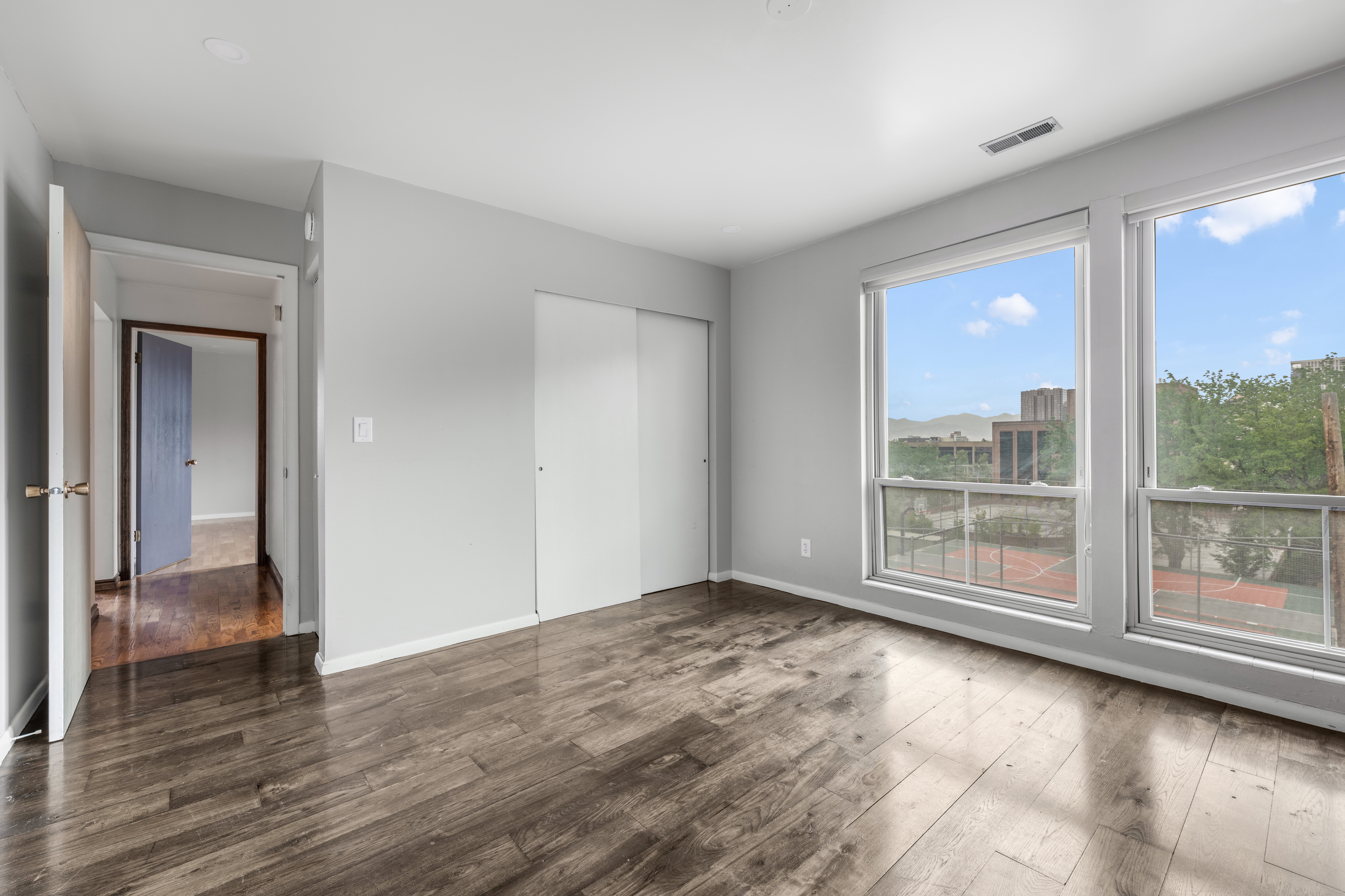 Spacious room featuring wood-finish flooring, light grey painted walls, large windows, and white sliding closet doors