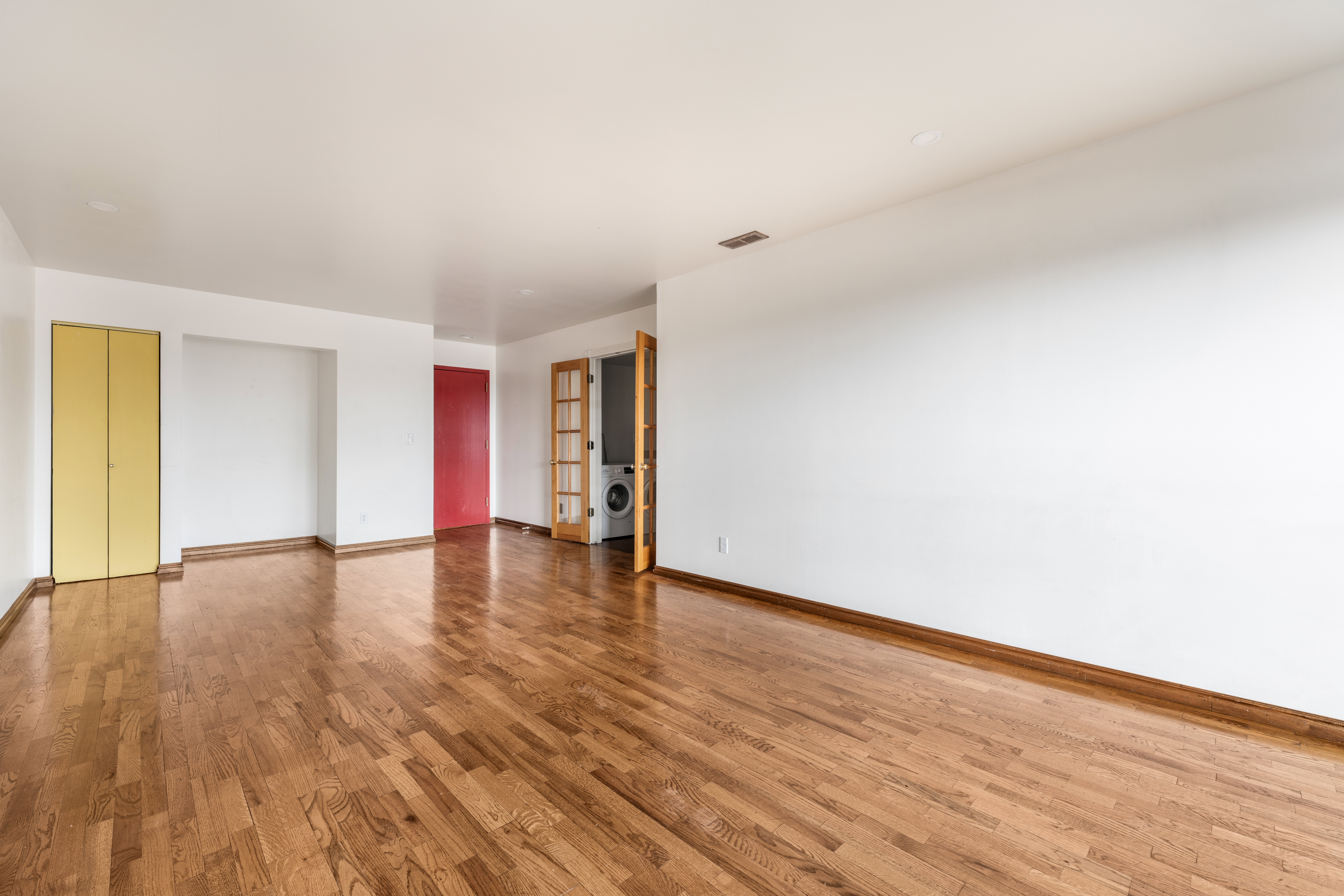 Open room featuring wood-finish flooring, white walls, and a recessed ceiling vent