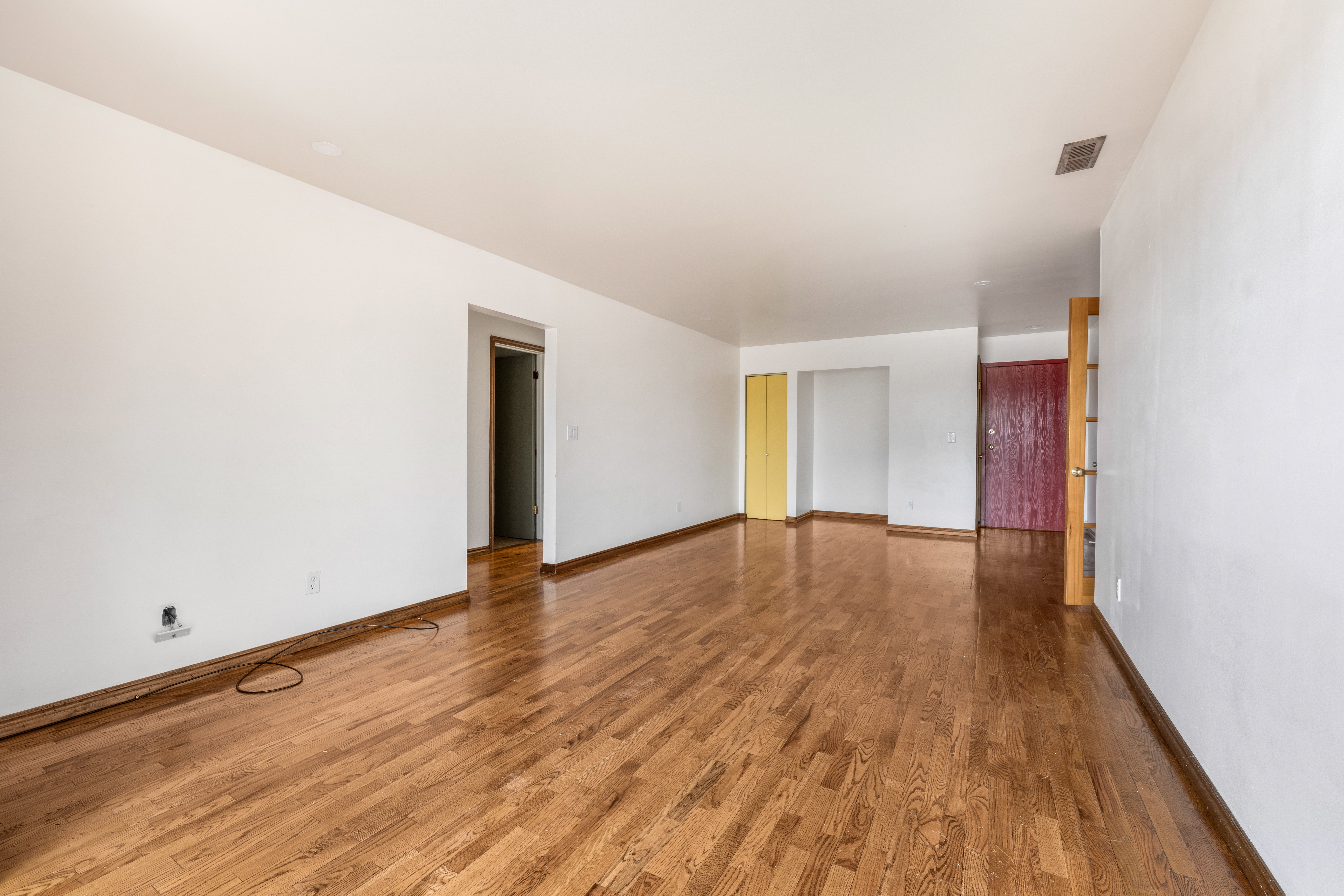 Spacious living area featuring rich wood-finish flooring, crisp white walls, and a recessed ceiling vent