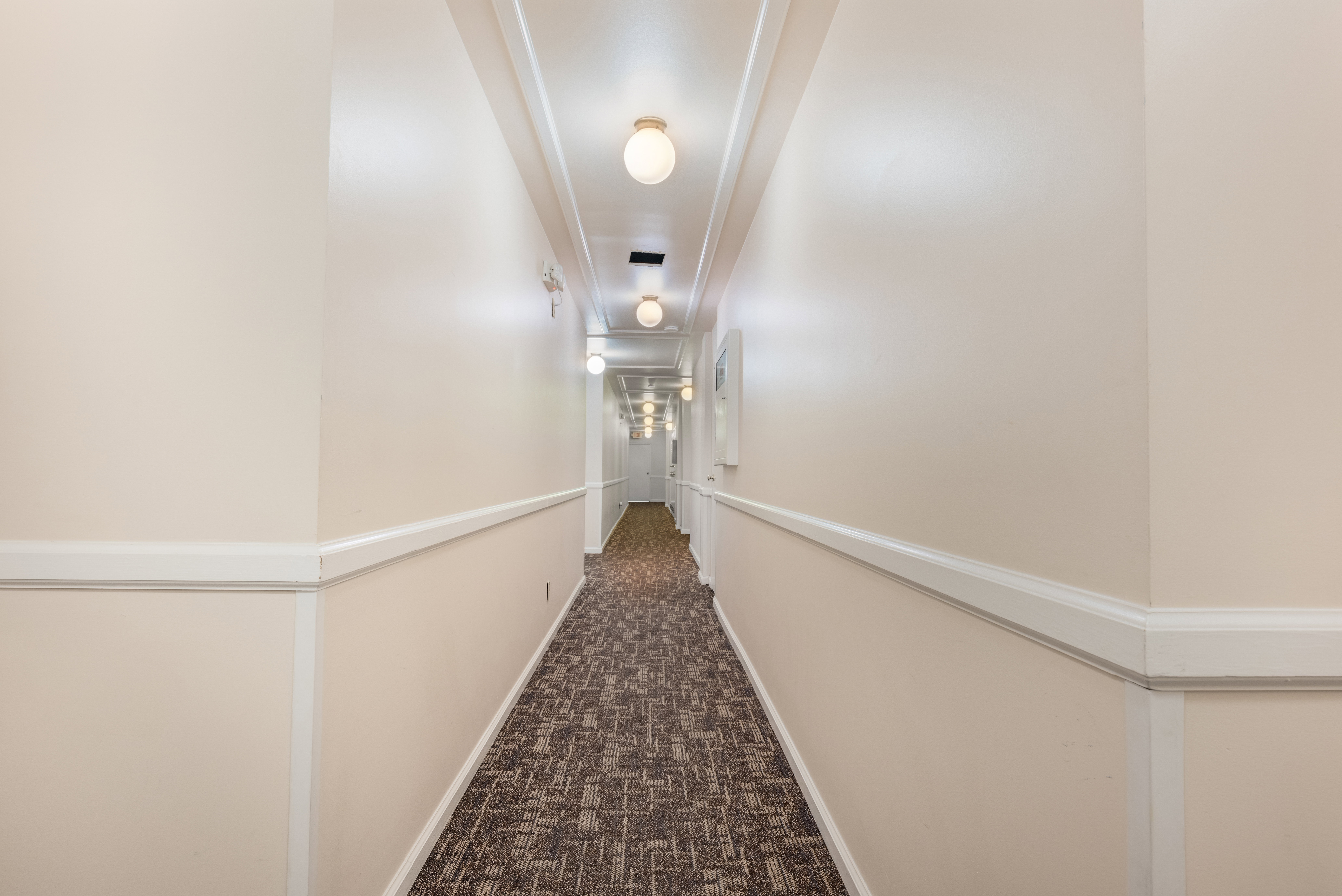 Long hallway featuring wainscoting, crown molding, patterned carpet flooring, and globe ceiling lights
