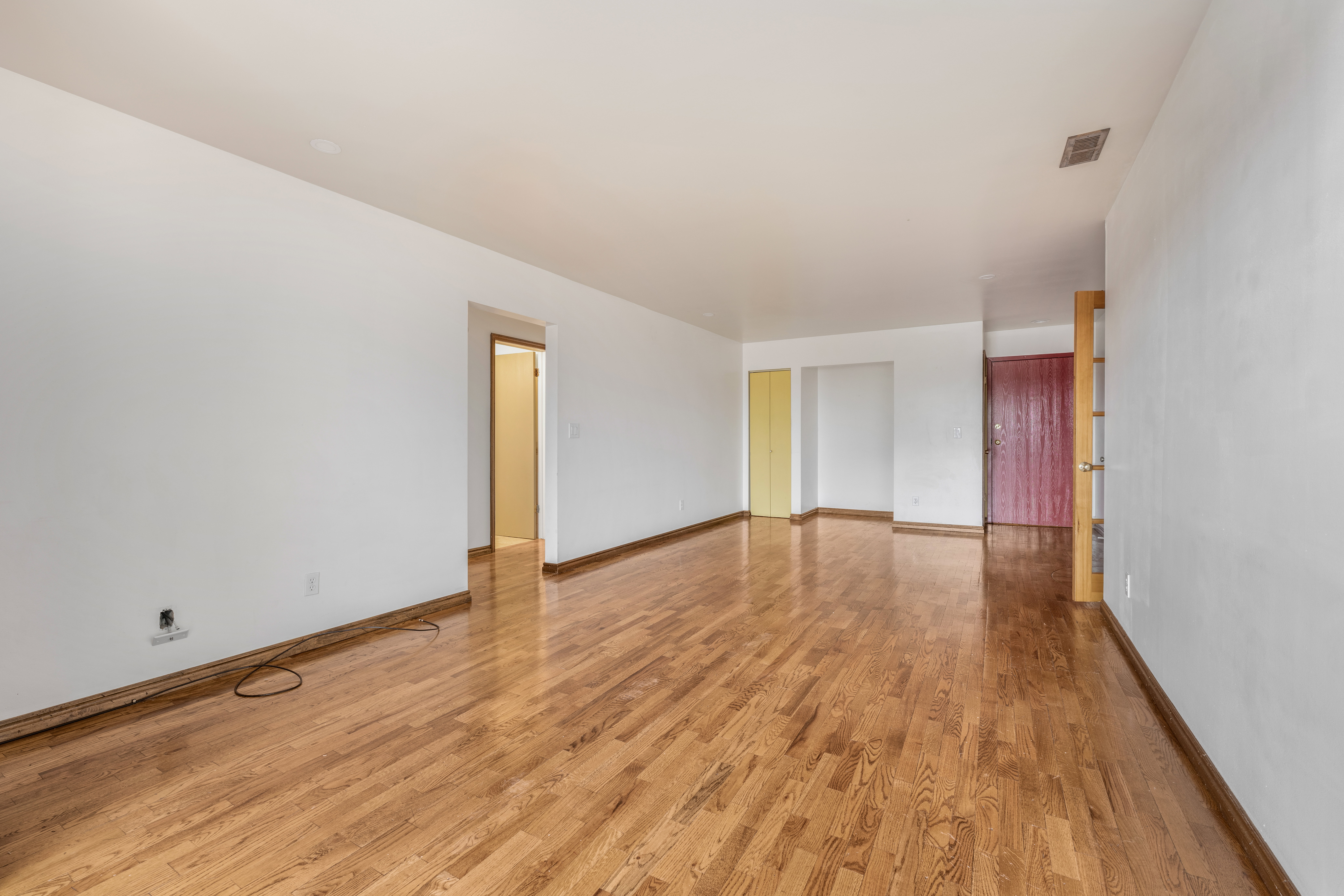 Spacious room featuring wood-finish flooring, white walls, and bright overhead lighting