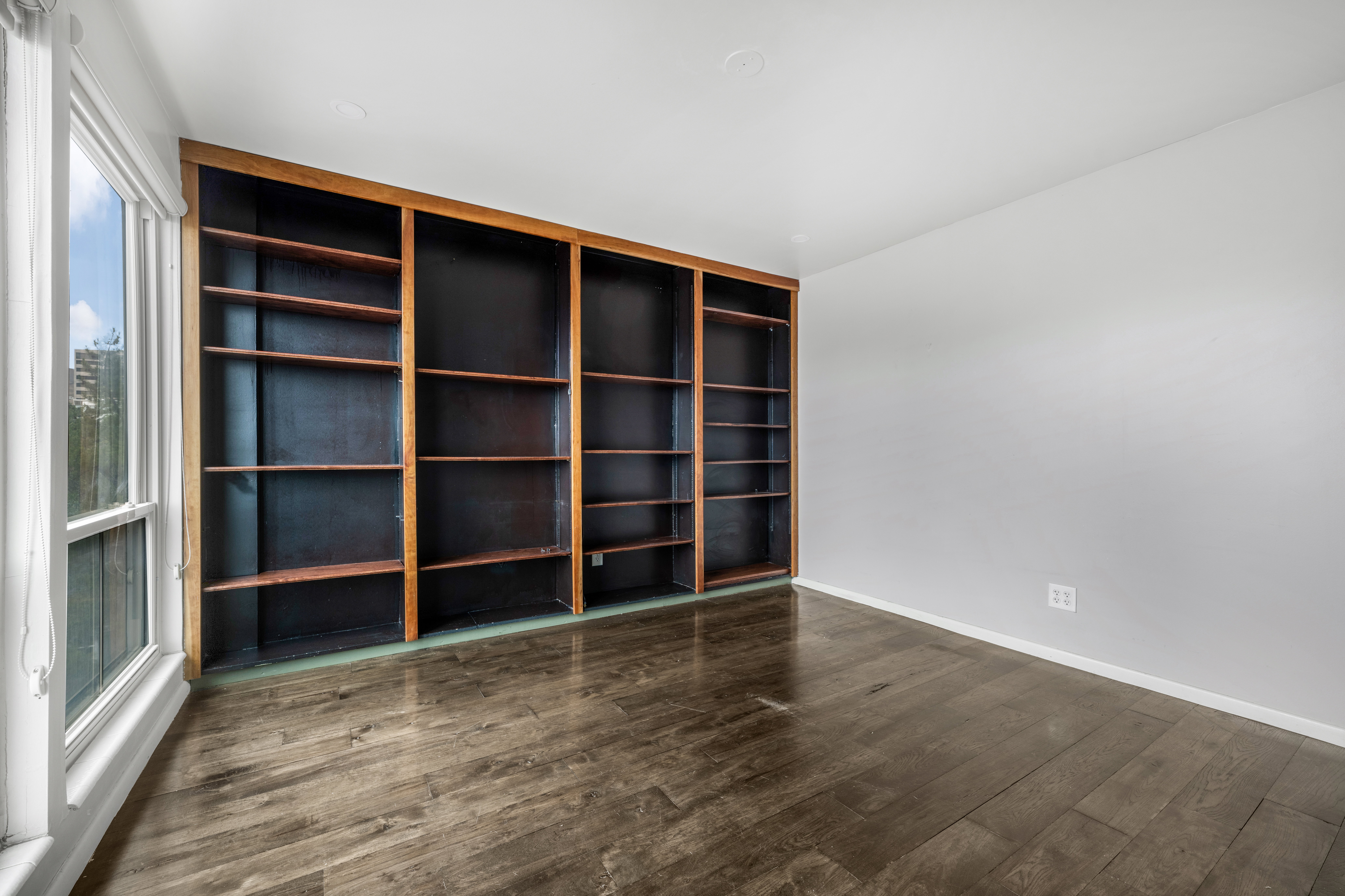 Spacious room featuring extensive built-in shelving, hardwood-style flooring, a large window, and neutral wall tones