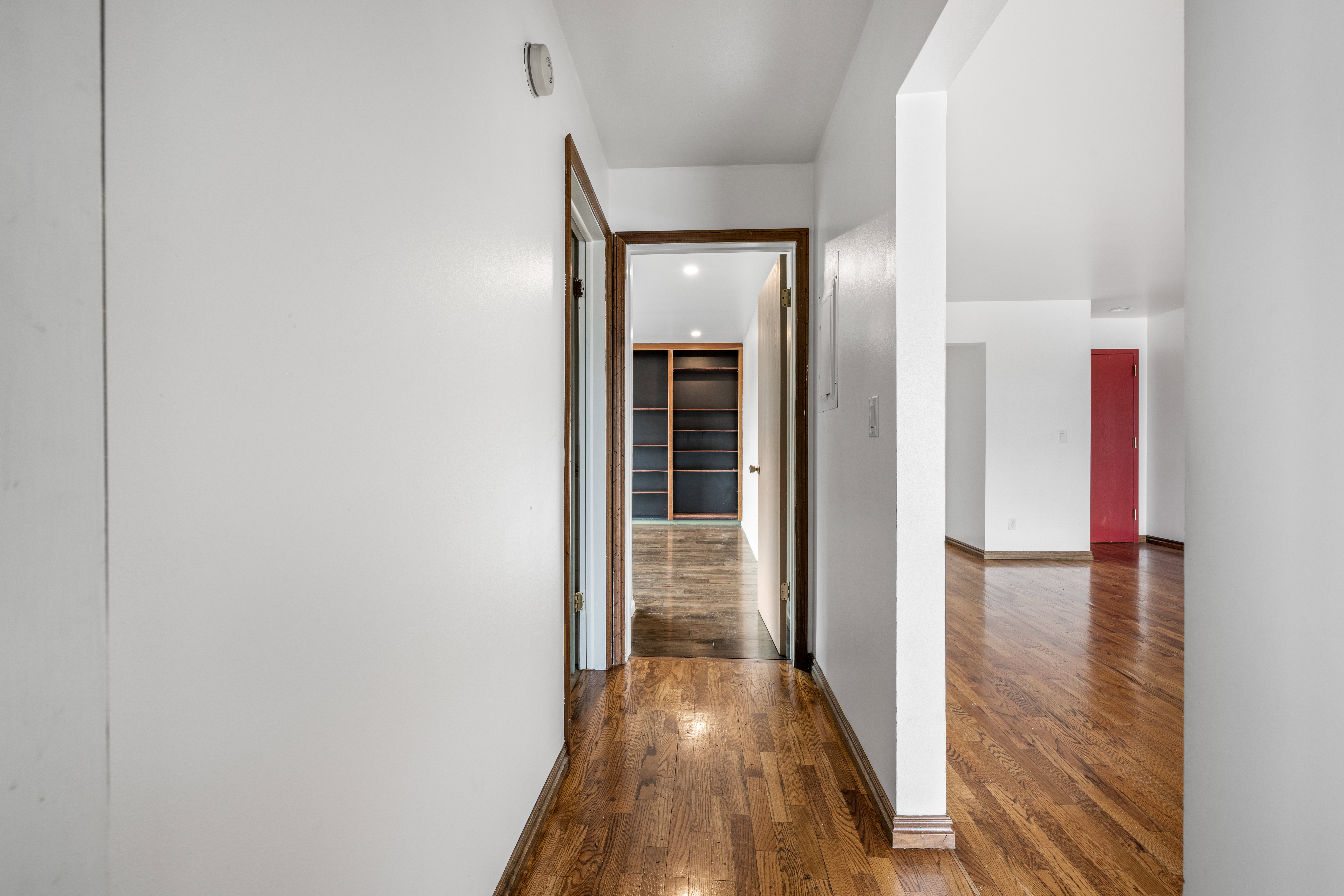 Hallway featuring polished wood-finish flooring, white walls, and wood-trimmed doorways