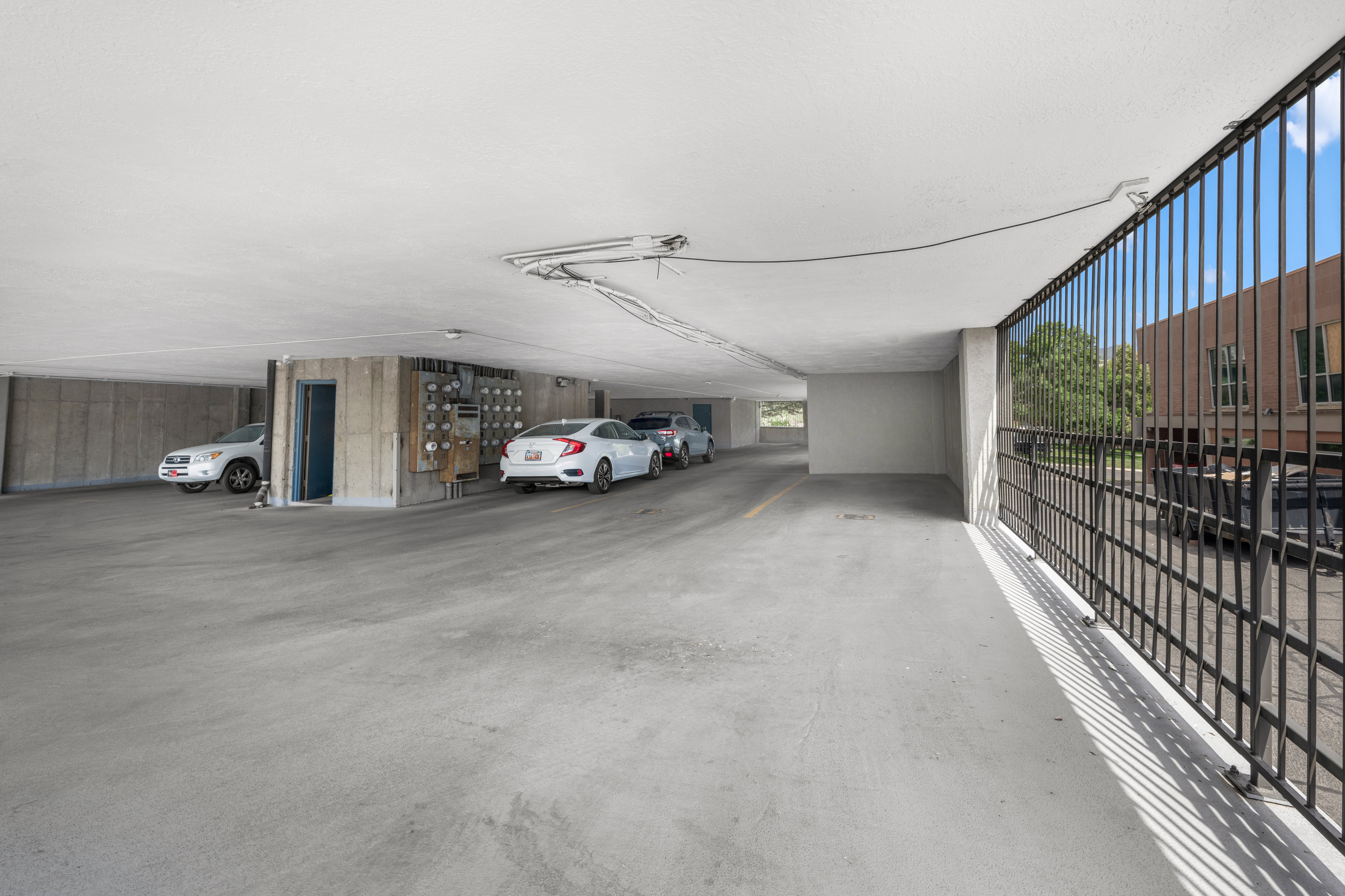 Covered parking area featuring concrete flooring, concrete walls, and overhead lighting