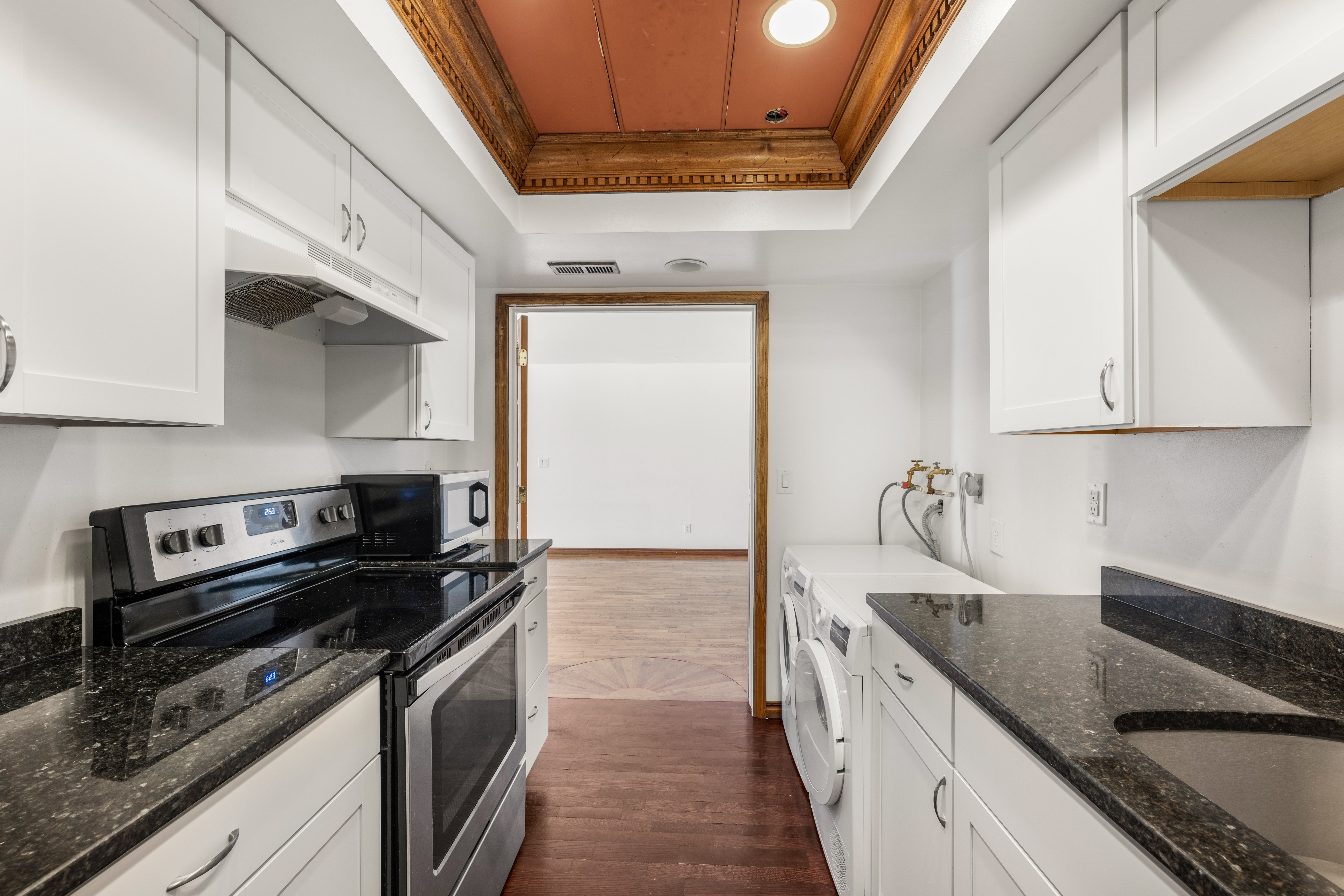 Galley kitchen with white cabinetry, dark stone countertops, stainless steel appliances, and wood-finish flooring