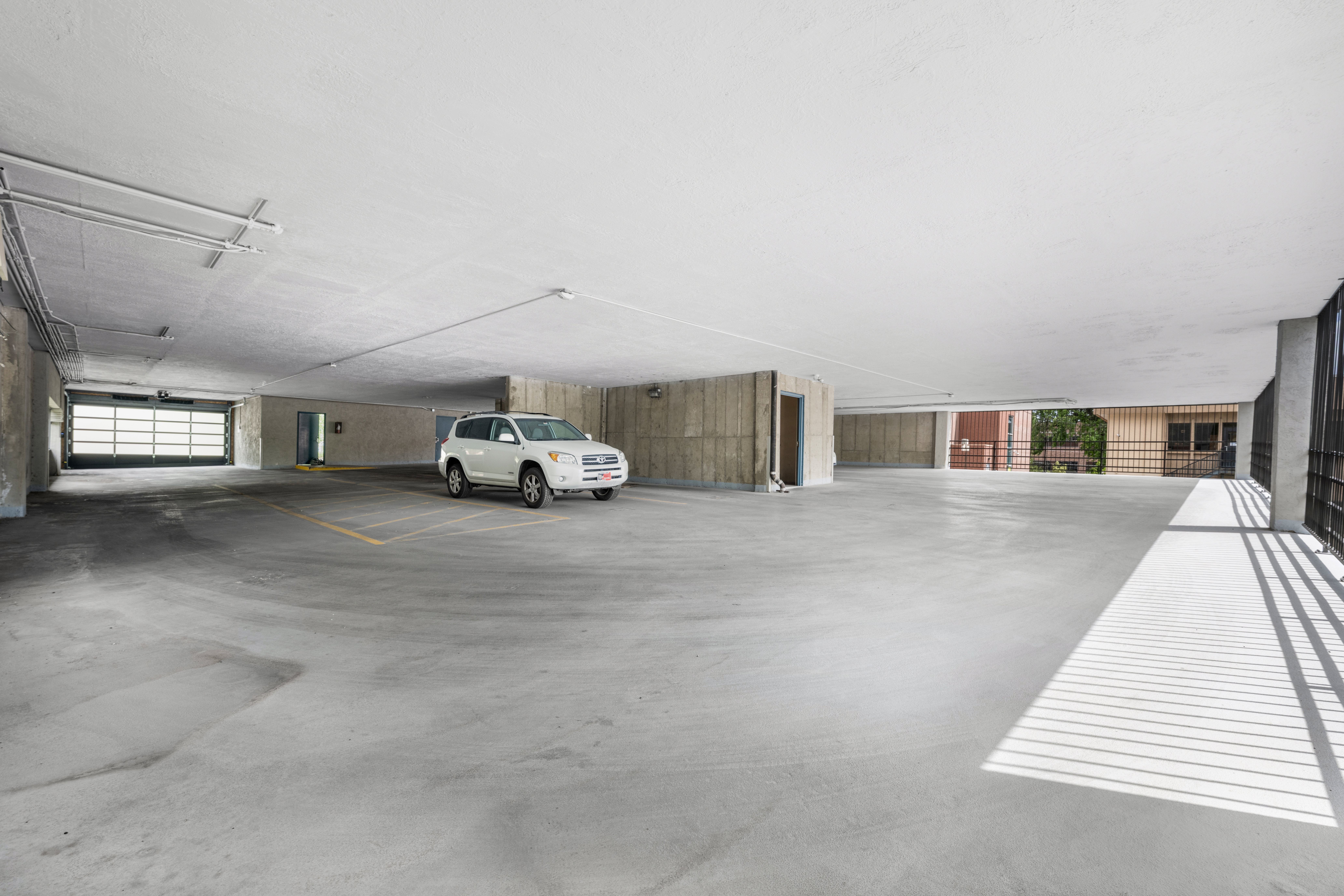 Spacious underground parking garage featuring concrete flooring, a large roll-up entry door, and exposed conduit