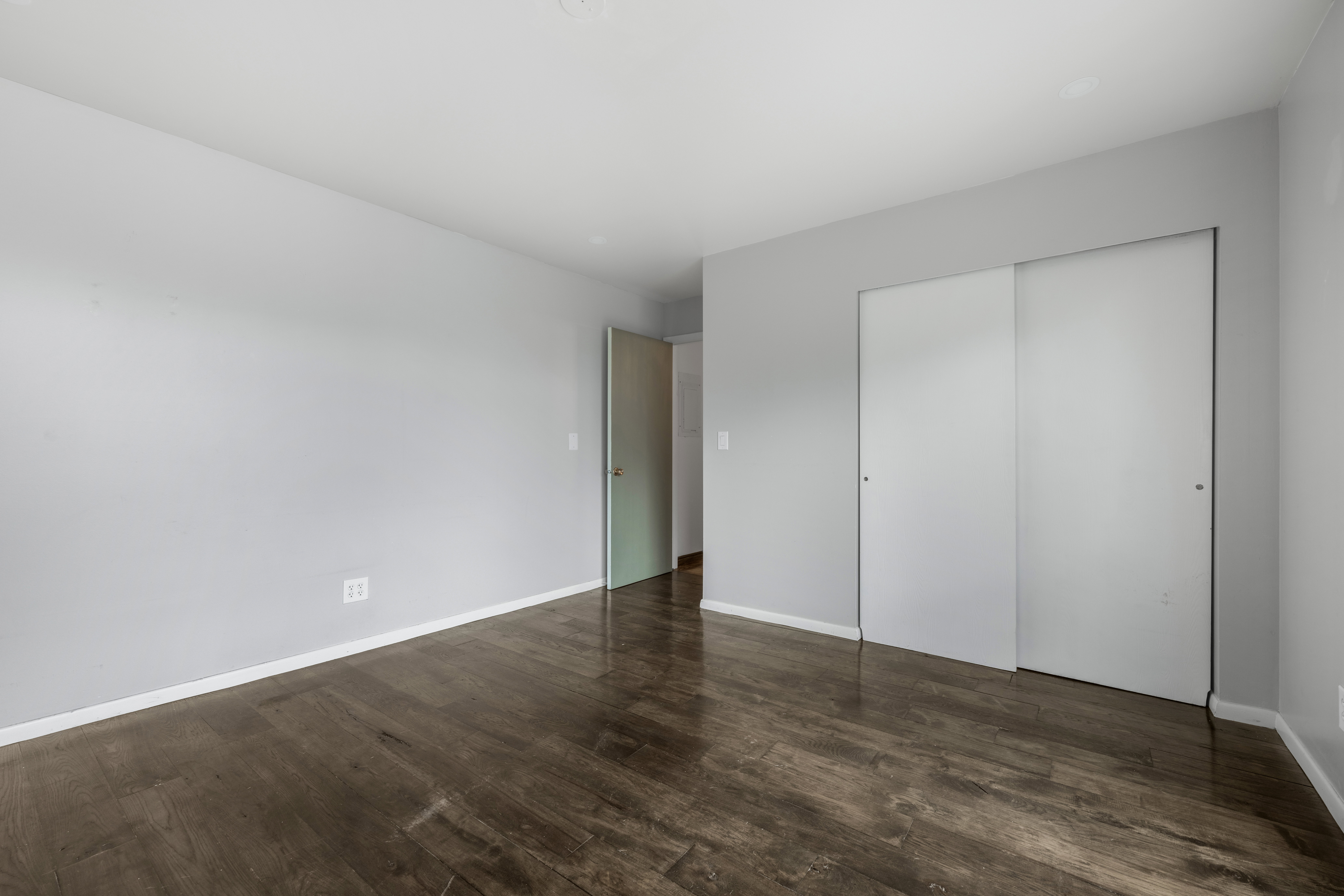 Spacious room featuring wood-finish flooring, light gray walls, white baseboards, and a built-in closet with sliding doors