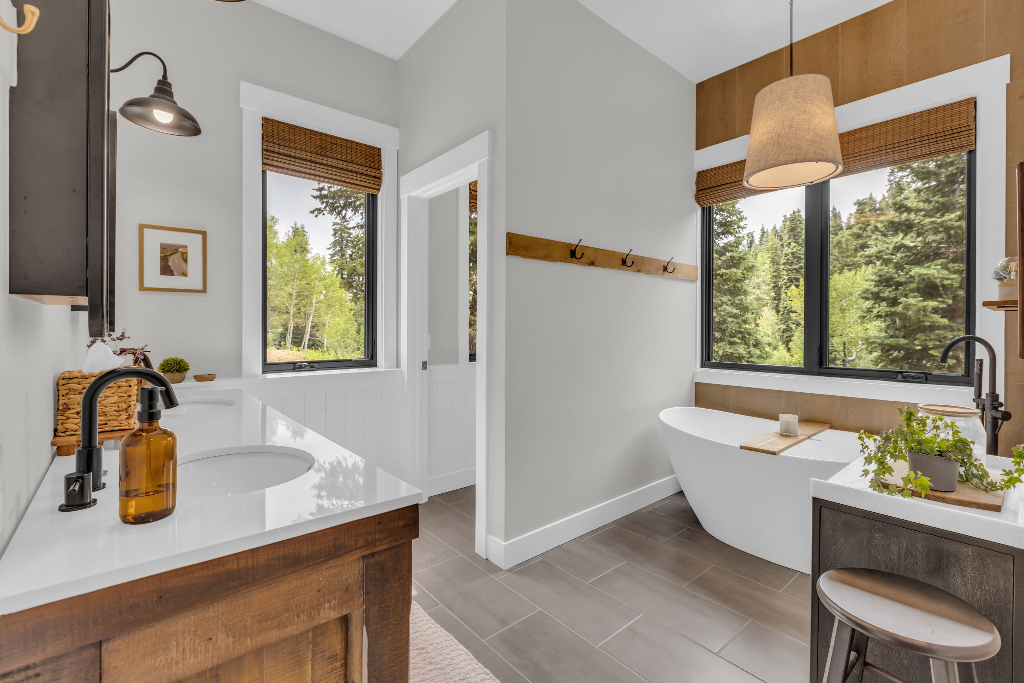 Bathroom featuring a freestanding soaking tub, wood-finish flooring, two large windows with woven blinds, and a double vanity with stone countertops