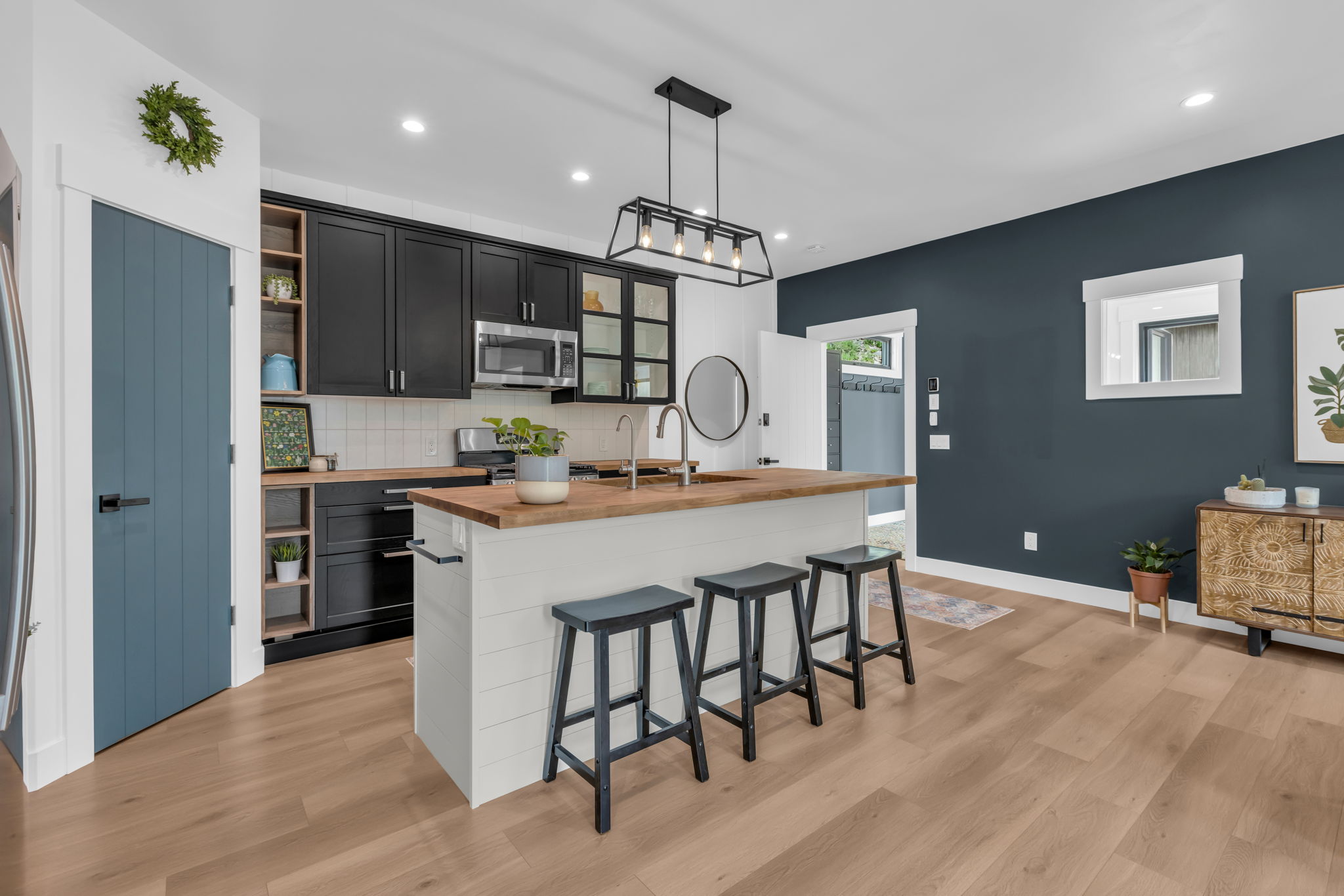 Contemporary kitchen featuring black cabinetry, light wood-finish countertops, stainless steel appliances, and a central island with bar seating