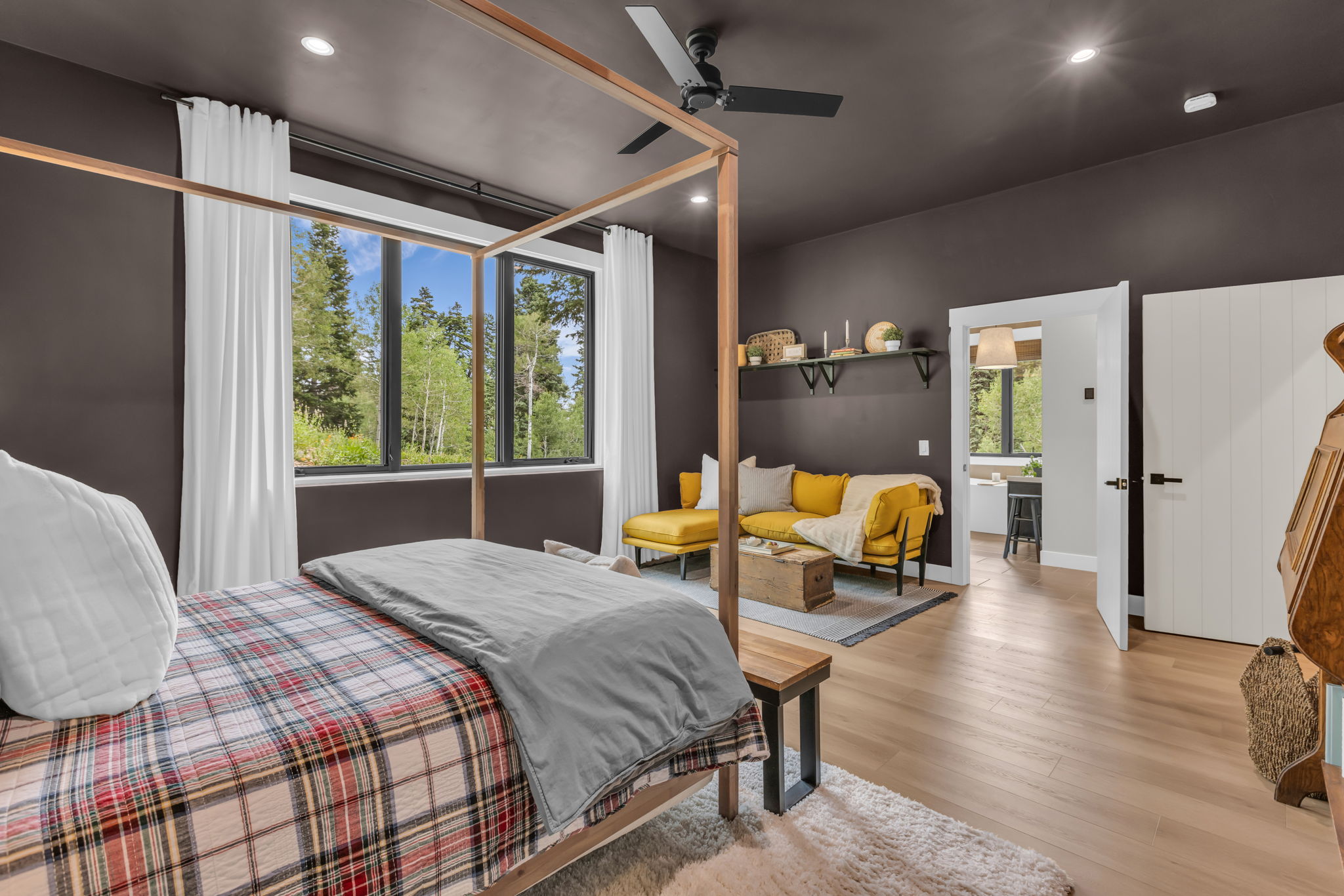 Expansive windows with black trim, dark accent walls, light wood-finish flooring, a built-in ceiling fan, and recessed lighting