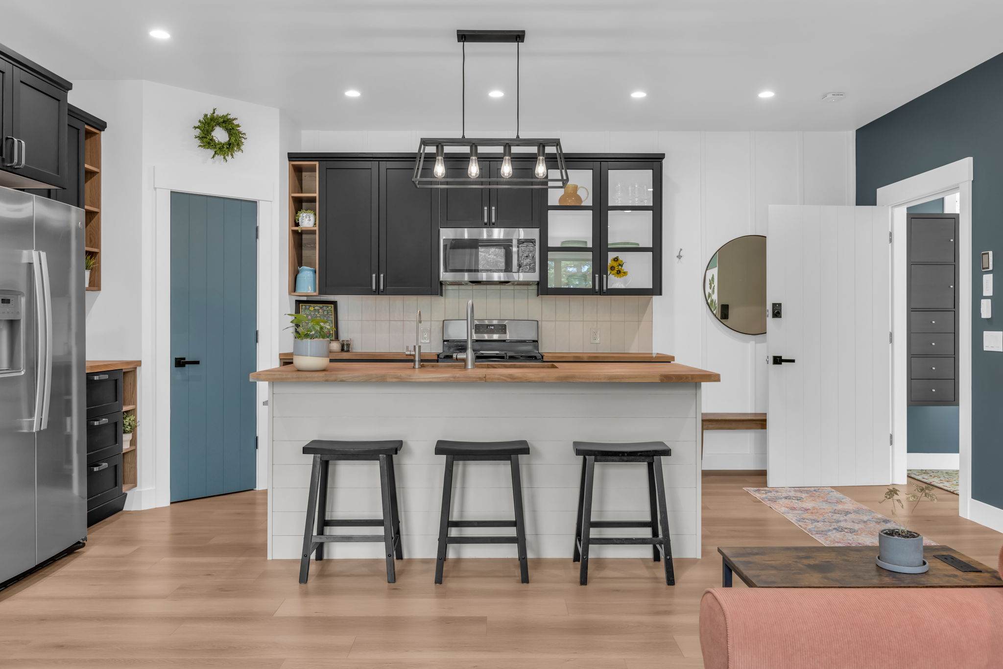 Modern kitchen featuring black cabinetry, stainless steel appliances, a wood-finish countertop island, a geometric pendant light fixture, and light wood-finish flooring