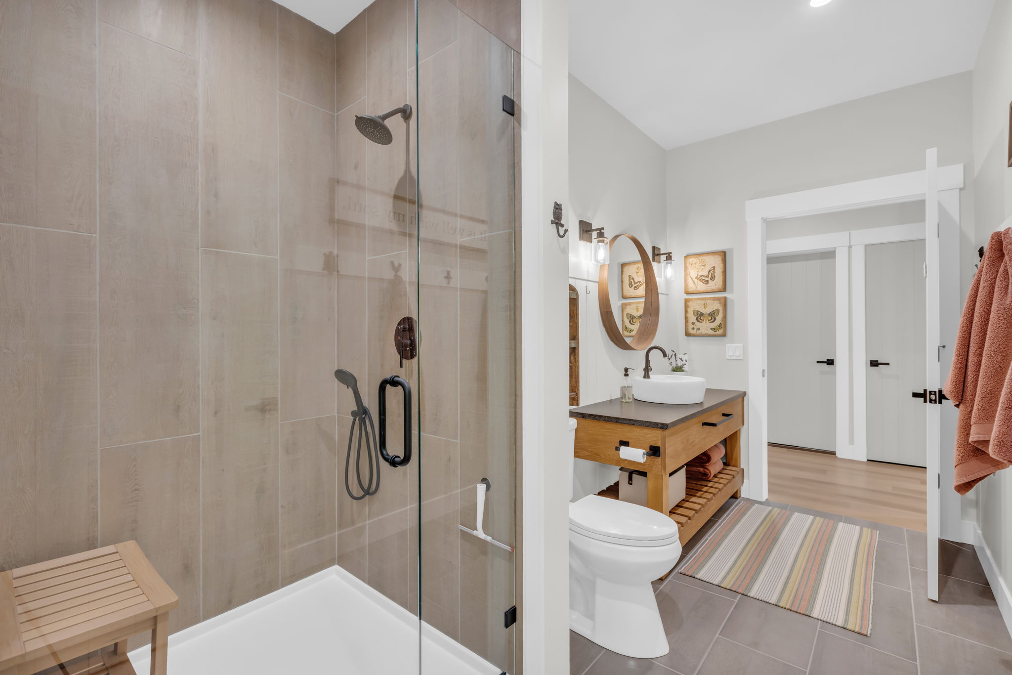 Walk-in shower with full-height tile surround and dark bronze fixtures, alongside a custom wood vanity with a vessel sink and dark countertop