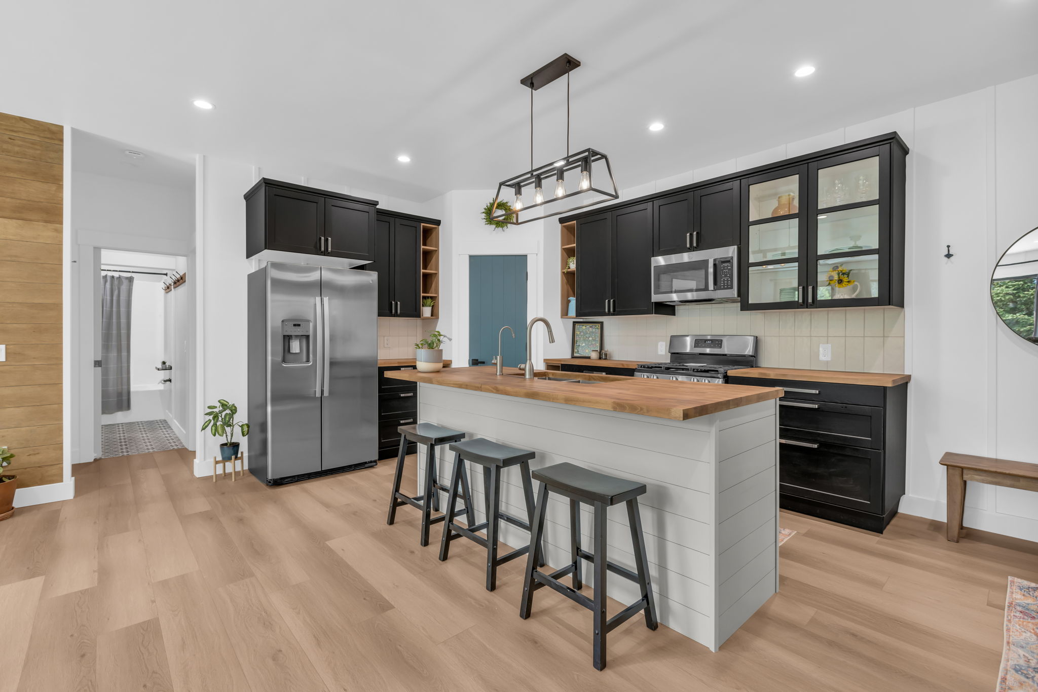 Kitchen featuring a central island with wood-finish countertop, stainless steel appliances, black cabinetry, white shiplap island paneling, and wood-finish flooring