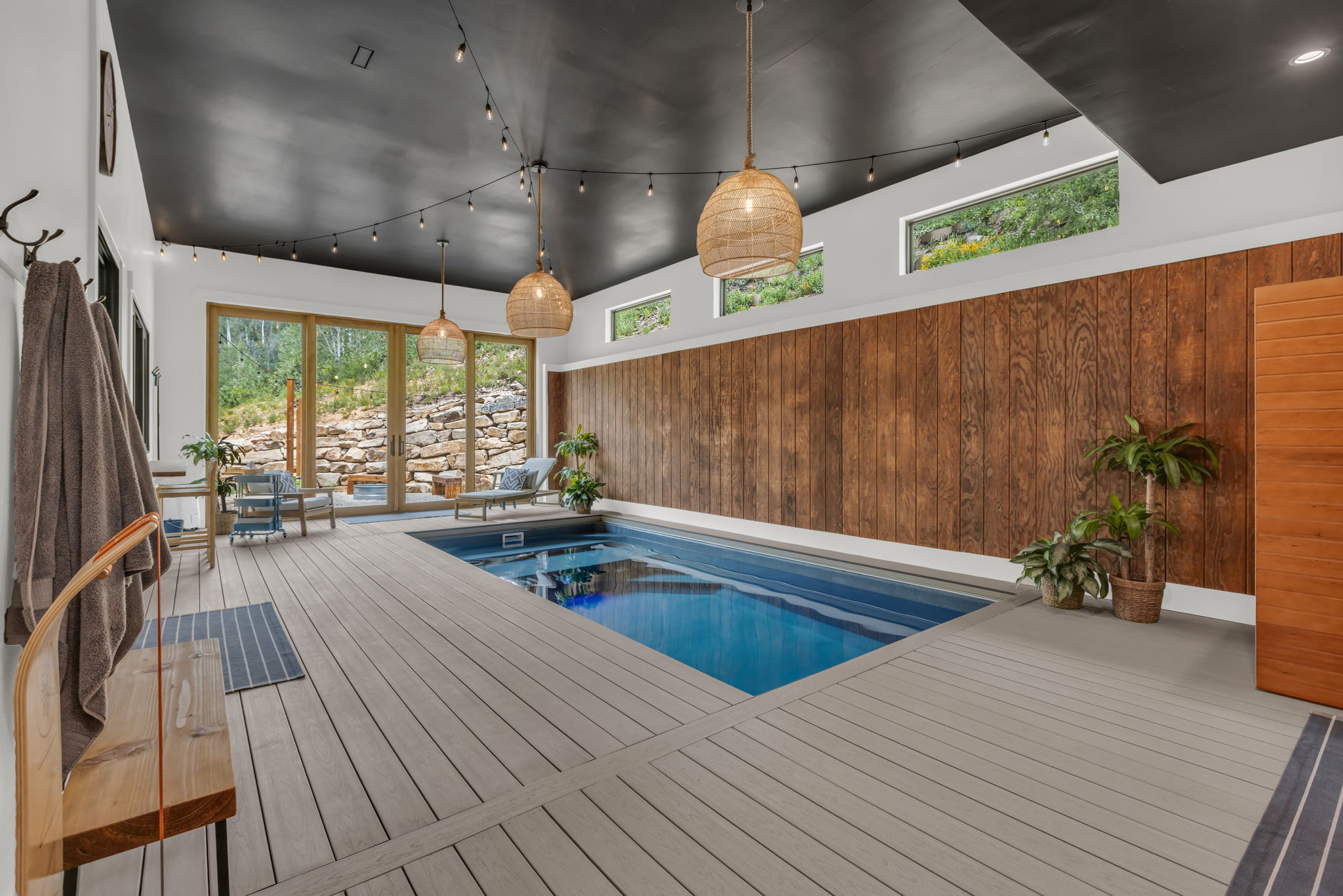 Indoor swimming pool with light-toned deck surround, framed by wood paneling and large glass doors