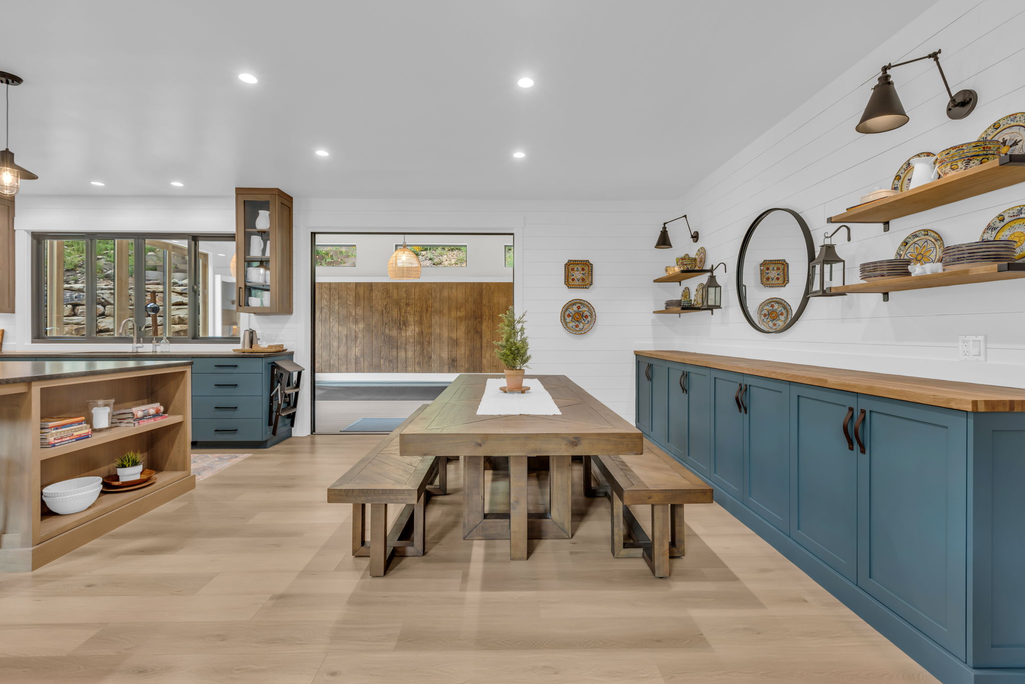 Open-concept interior featuring light wood-finish flooring, a dining area with a wood table and benches, and a custom built-in storage unit with blue cabinetry and wood-finish countertops