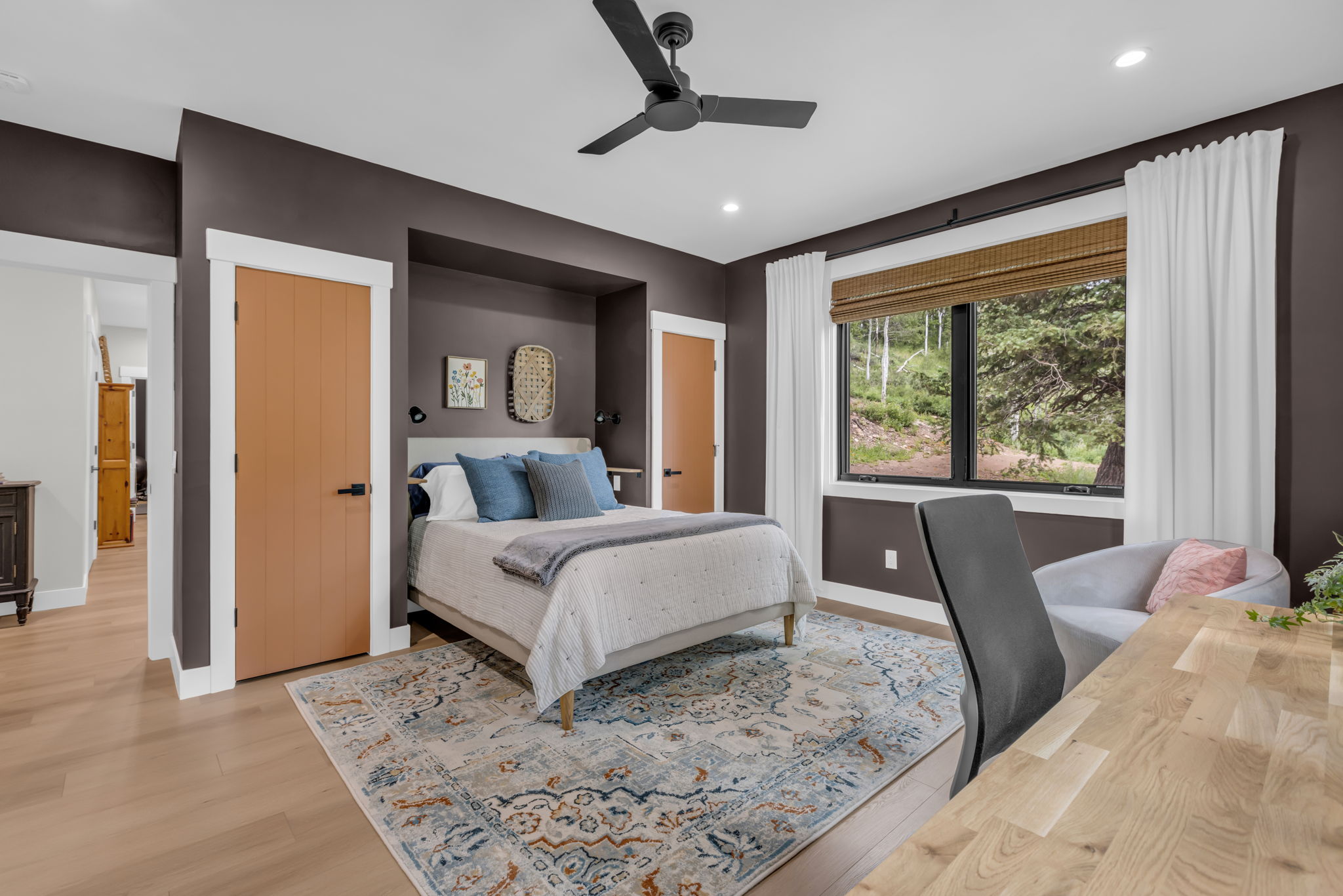 Bedroom featuring a large window with a natural landscape backdrop, light wood-finish flooring, and a modern ceiling fan