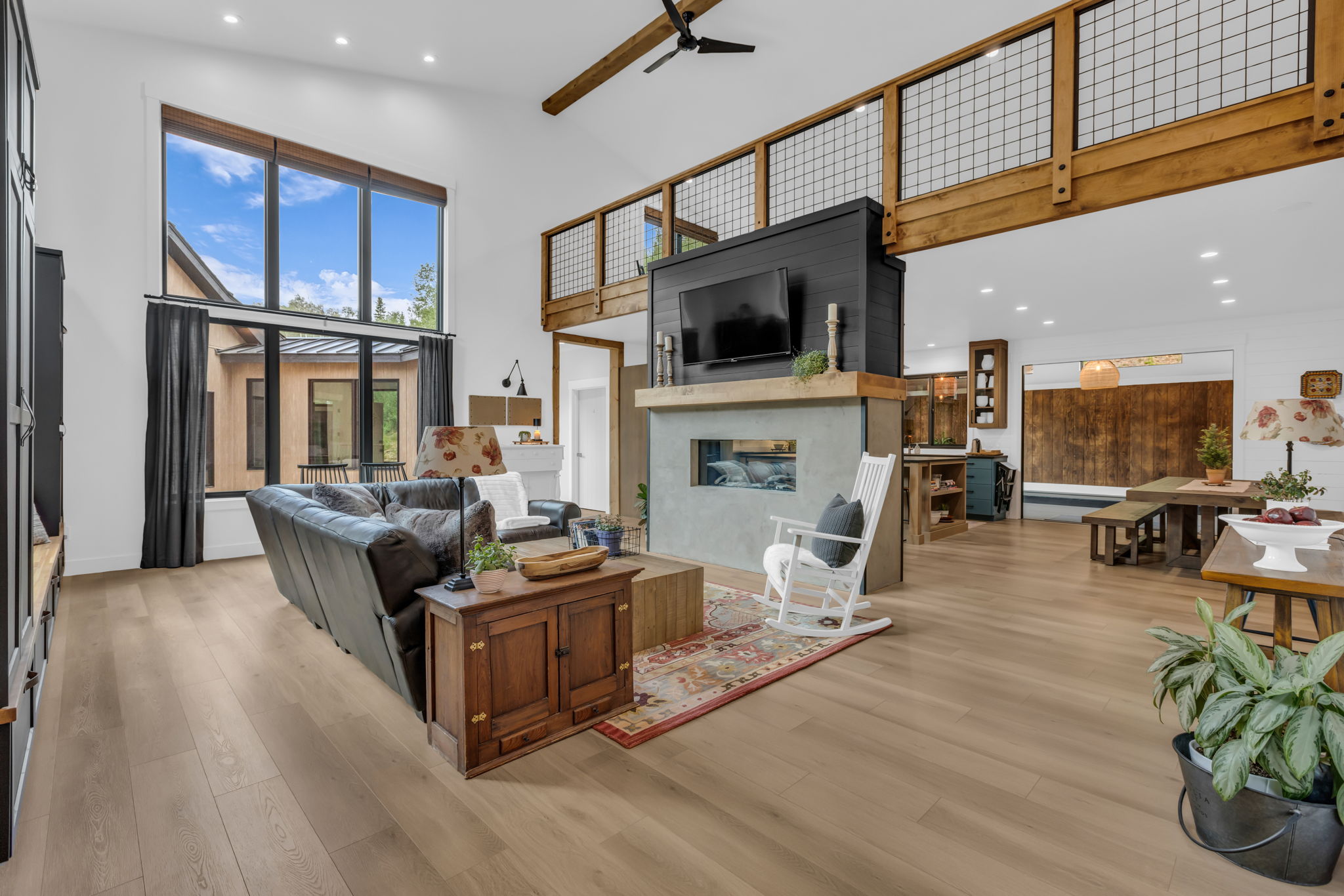 Spacious living area featuring high ceilings, wood-finish flooring, a contemporary fireplace with a concrete surround, large windows, and an exposed wood beam