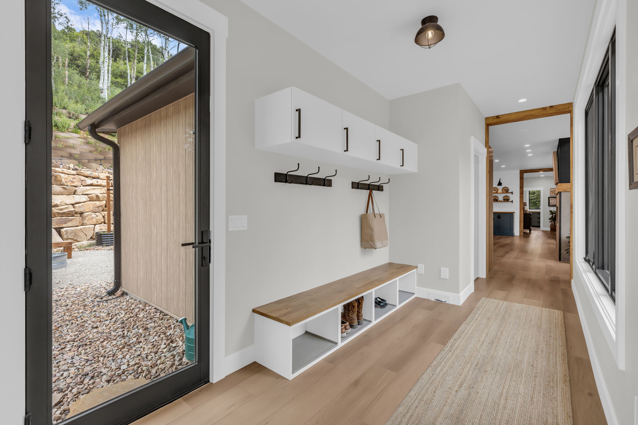 Entryway mudroom featuring integrated white cabinetry, wood-finish bench storage, multiple coat hooks, and durable light wood-finish flooring