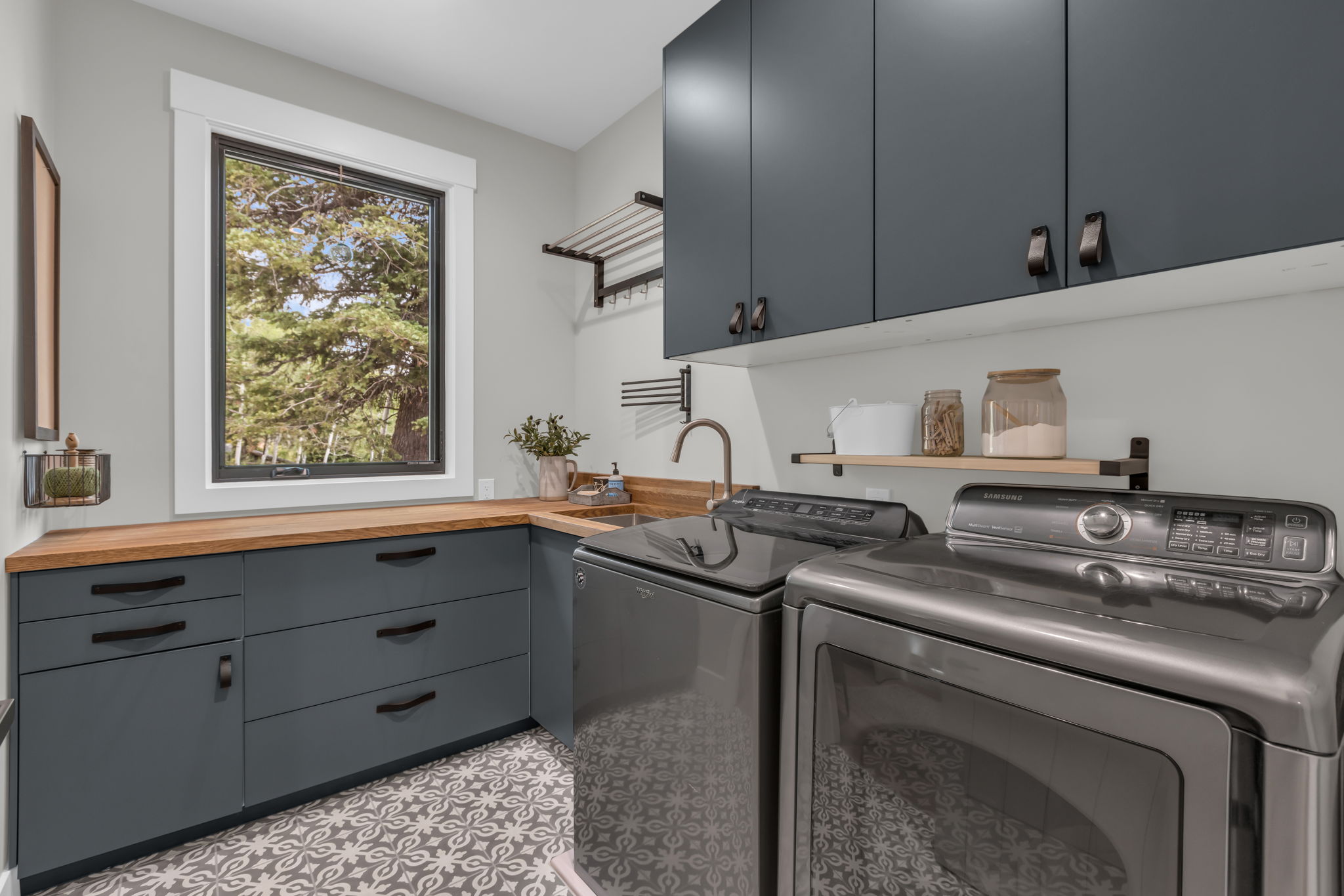 Laundry room featuring dark gray cabinetry, wood-finish countertops, and a patterned tile floor
