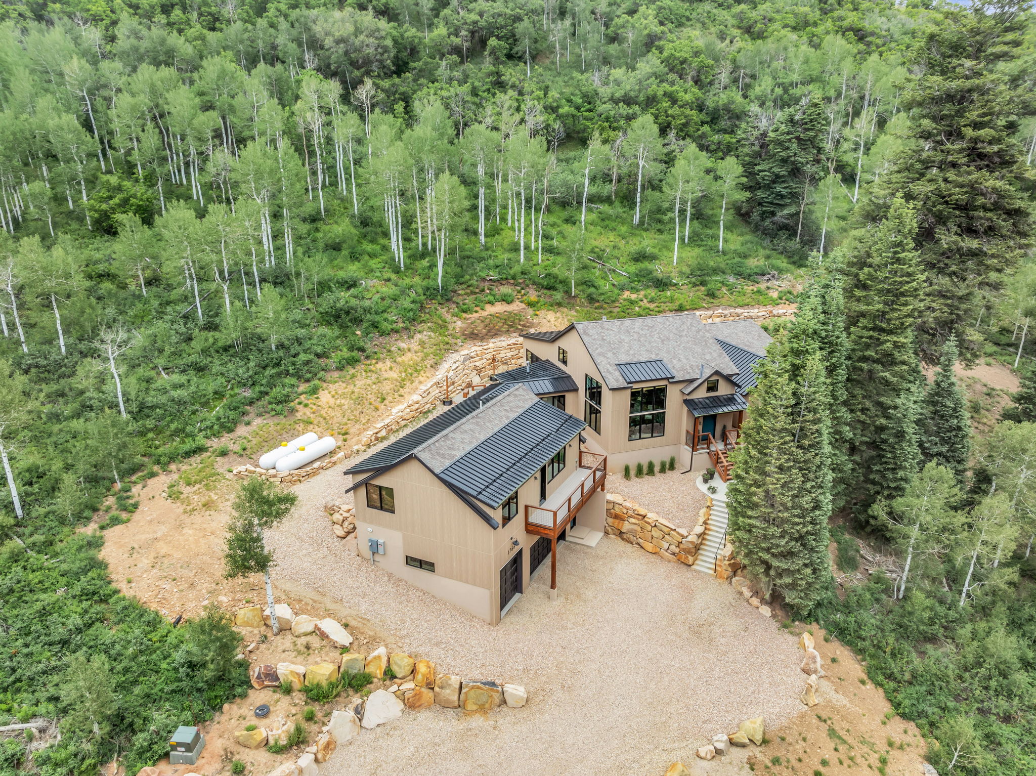 Modern mountain residence featuring a multi-level design, gravel driveway, and a natural stone retaining wall