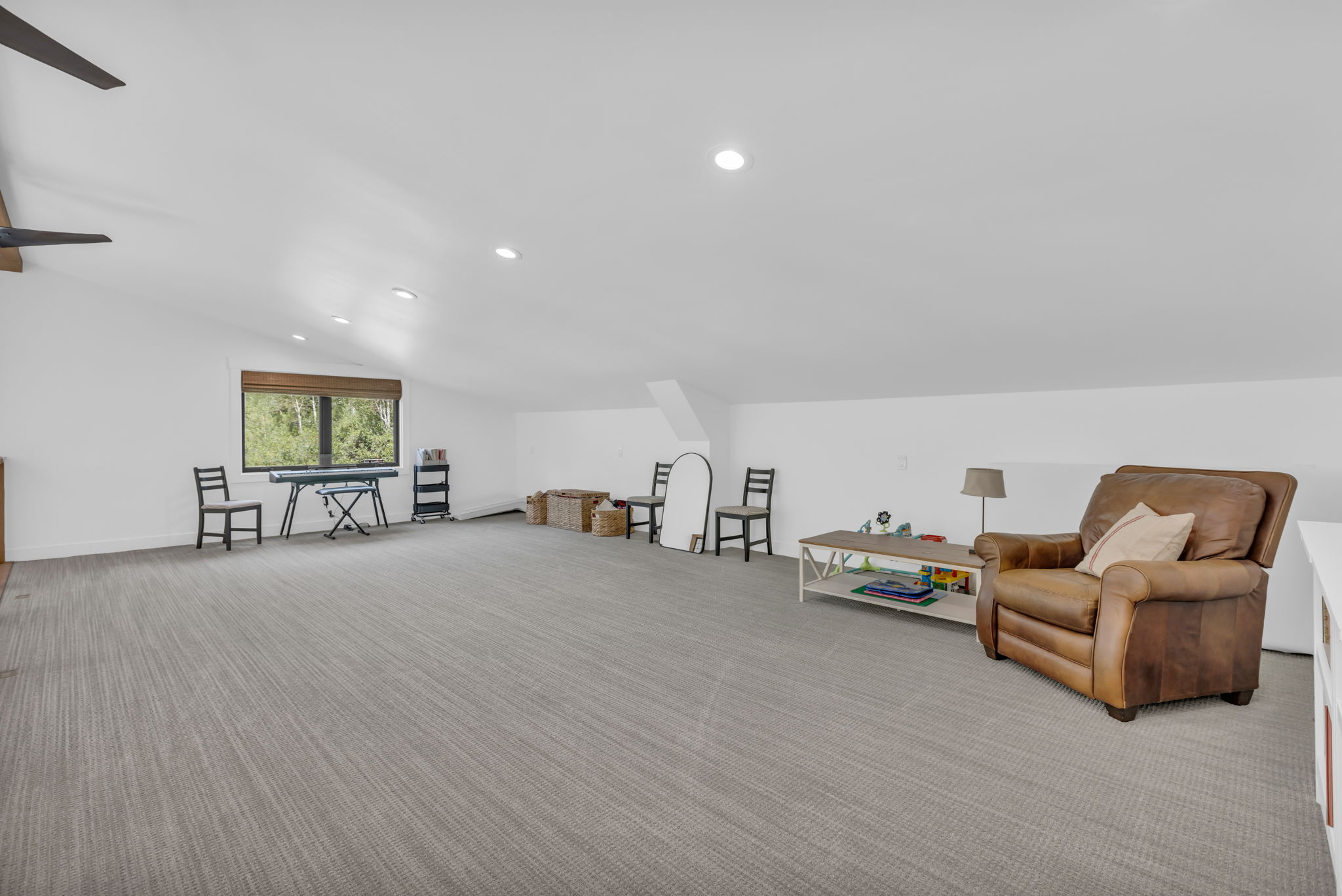 Spacious room featuring sloped ceilings, recessed lighting, and a large window with natural wood-finish blinds