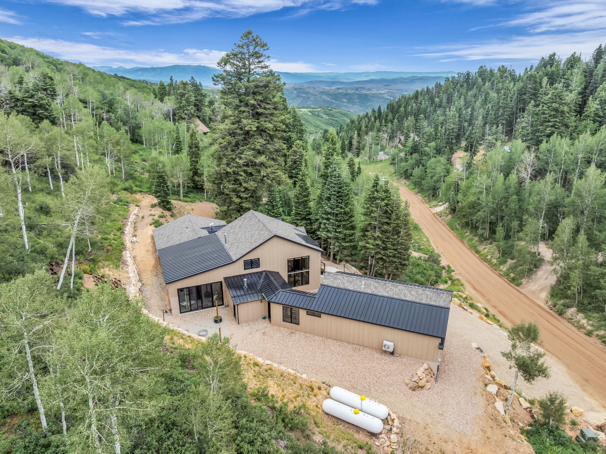 Modern mountain residence featuring a multi-level design with a natural wood-tone exterior, dark-frame windows, and a combination of shingle and metal roofing