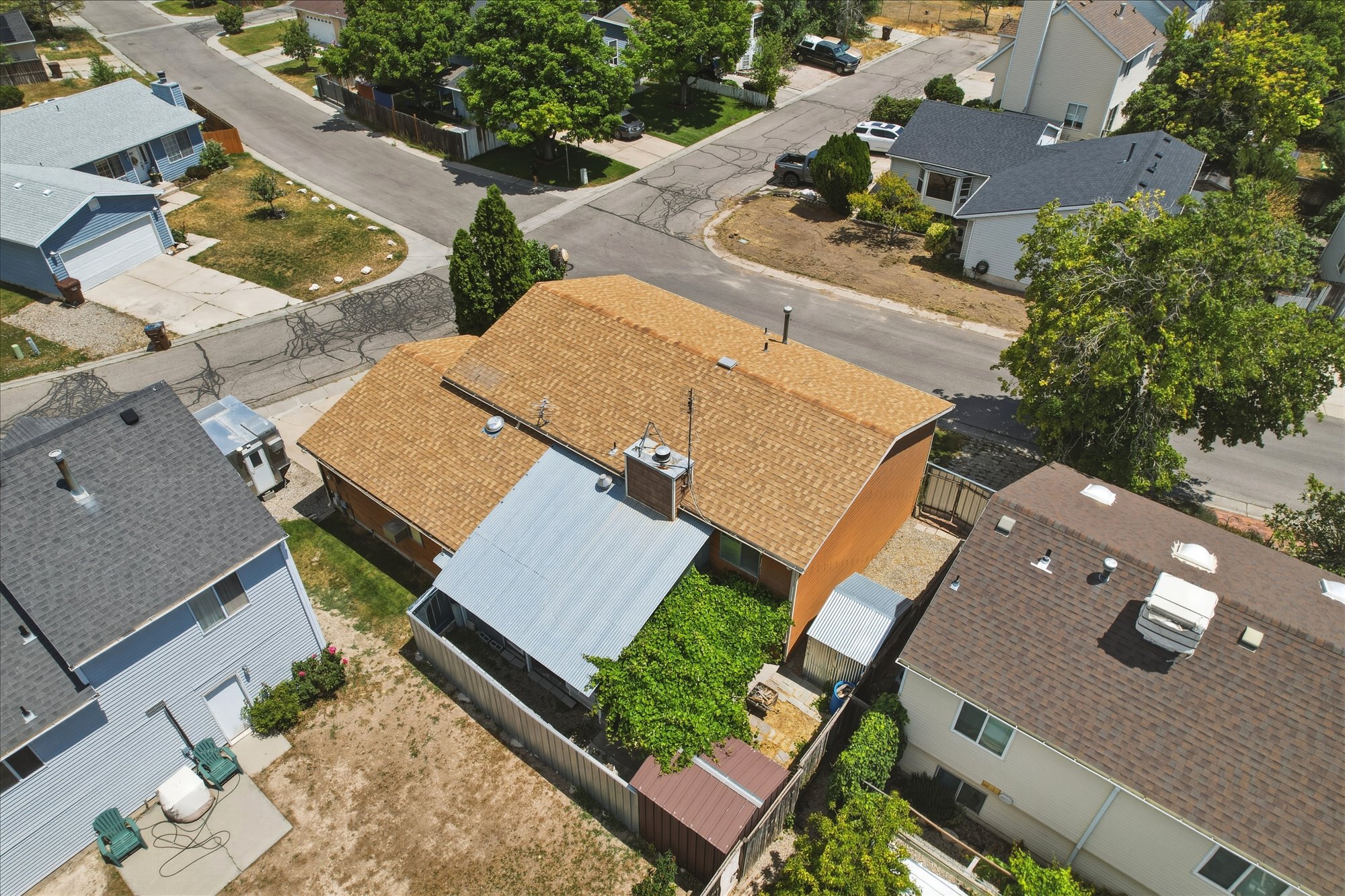 Brown shingle roof with a prominent chimney, surrounded by green landscaping and fencing