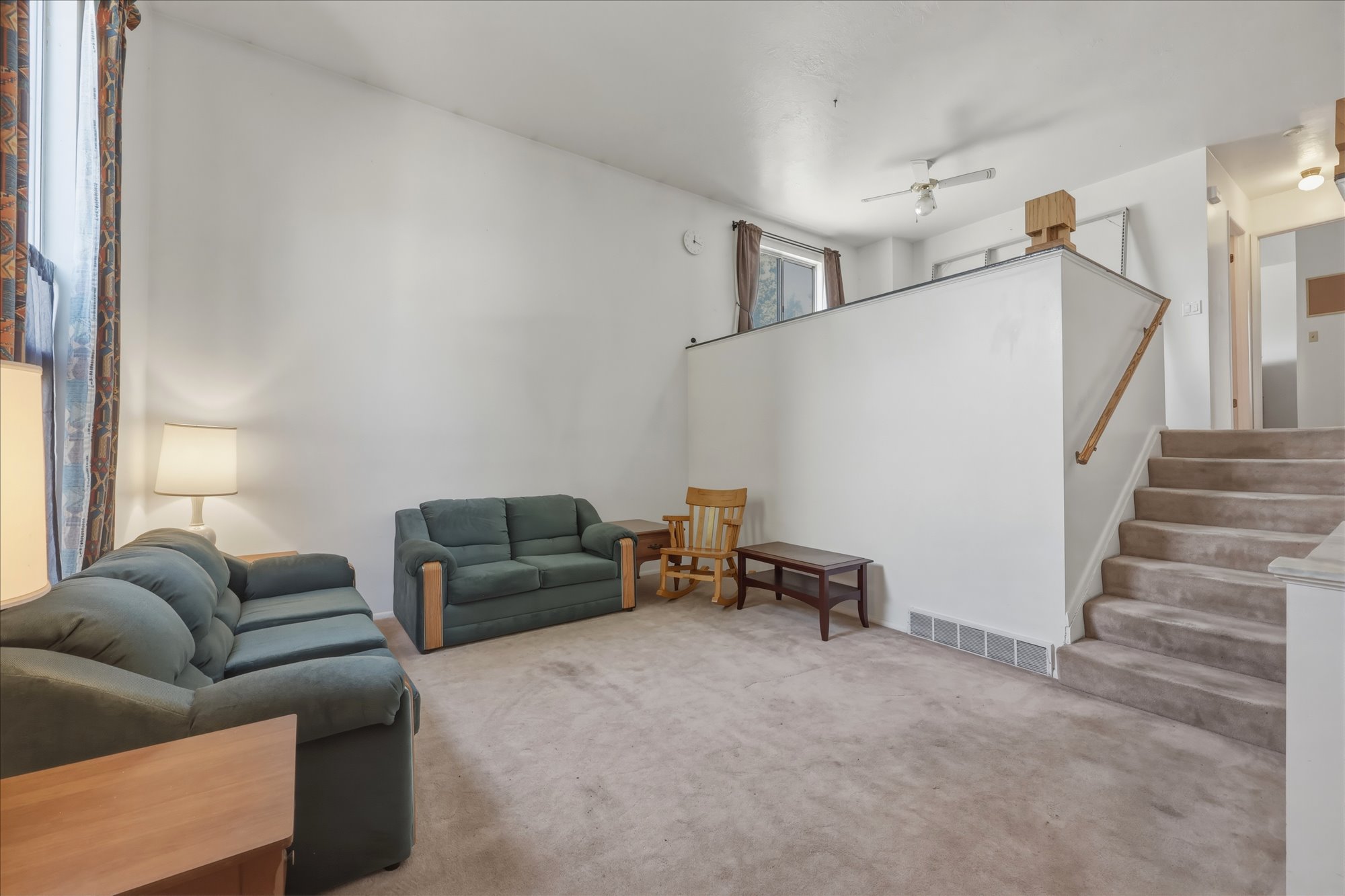 Carpeted living area featuring high ceilings, a window with drapery, and a carpeted staircase with a wood handrail