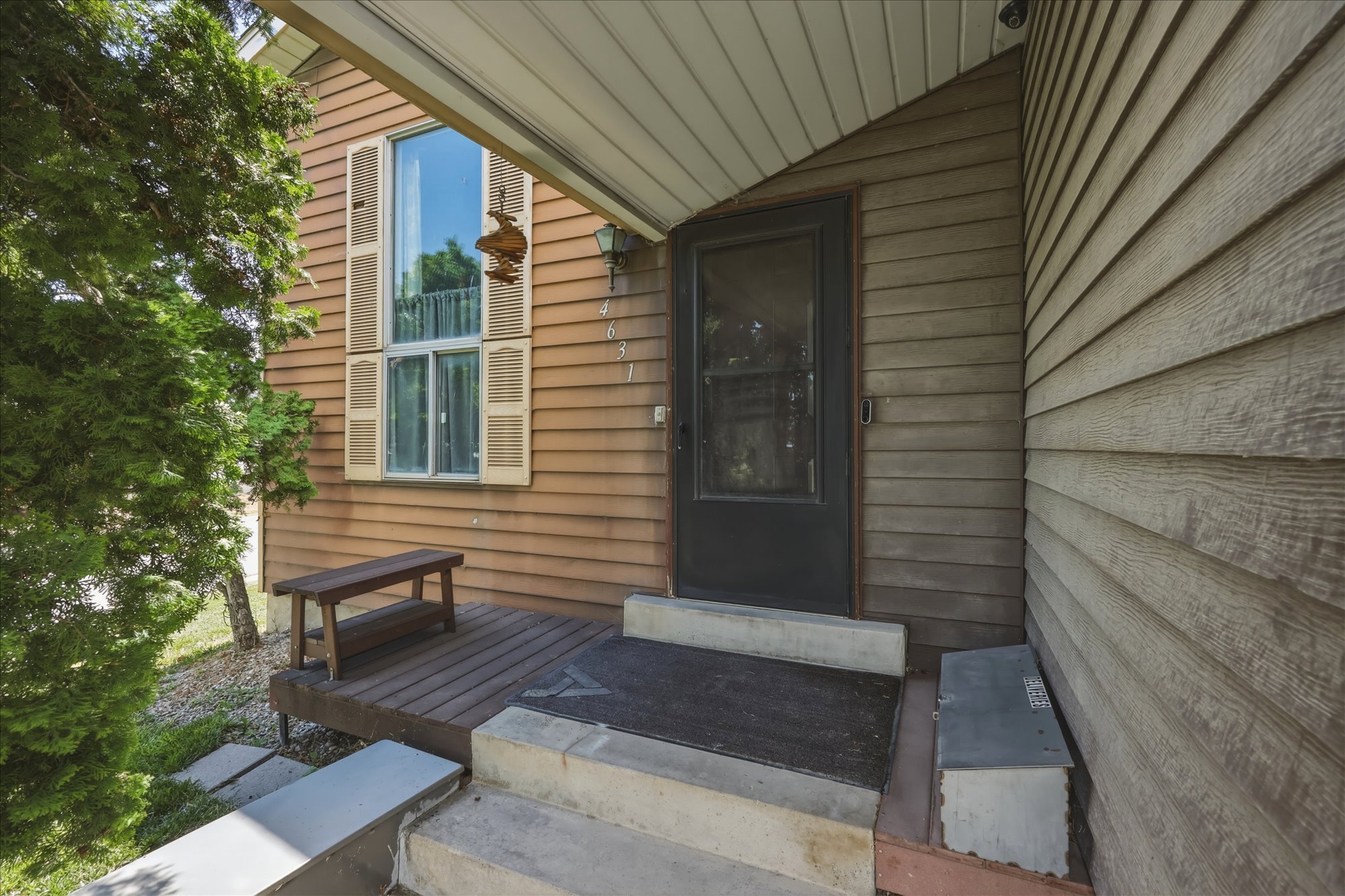 Front entrance featuring wood-finish siding, a dark screen door, a ground-level deck, and concrete steps