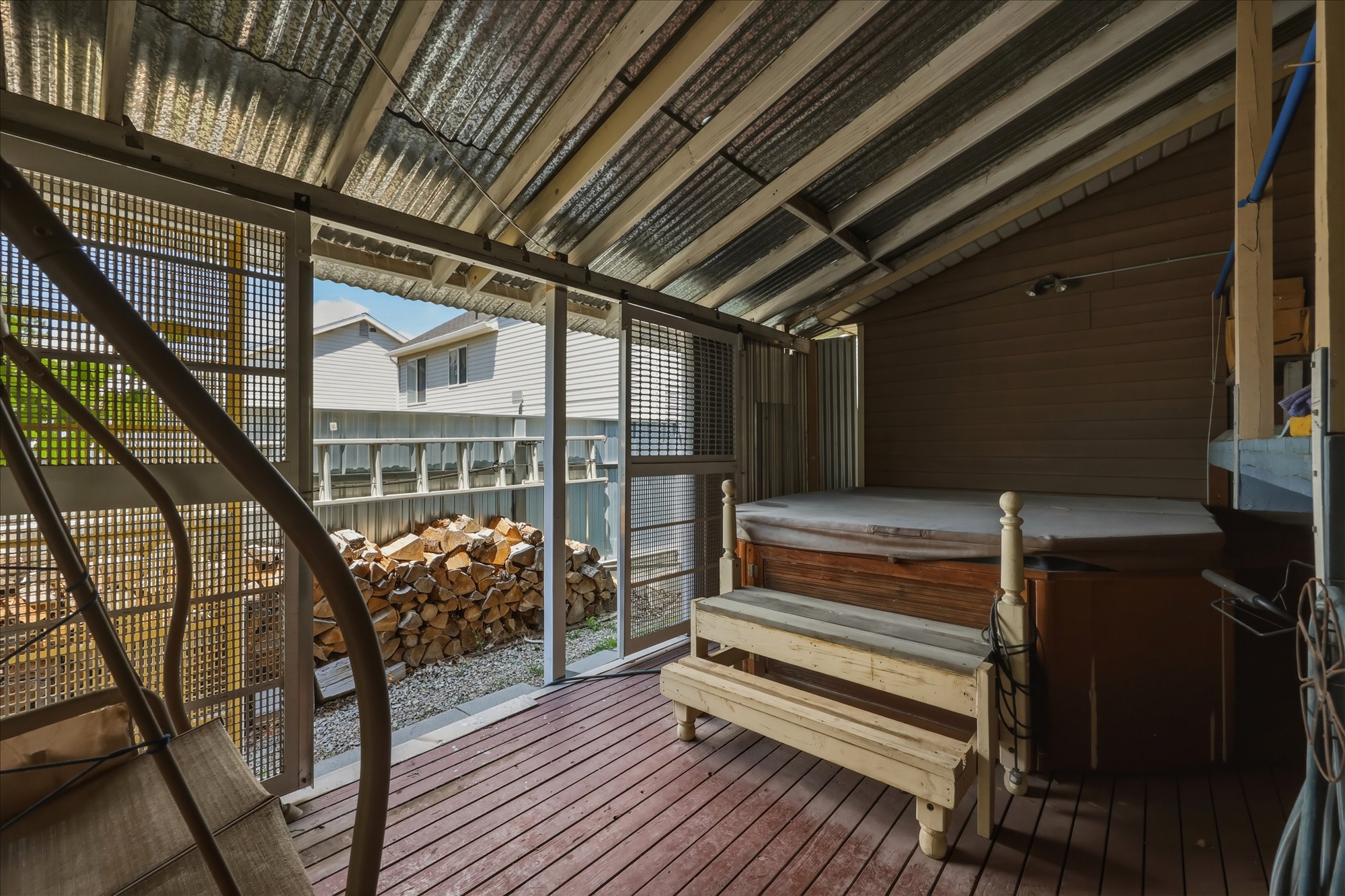 Covered outdoor area featuring a hot tub with wood surround, a slatted wood deck, and a corrugated metal roof
