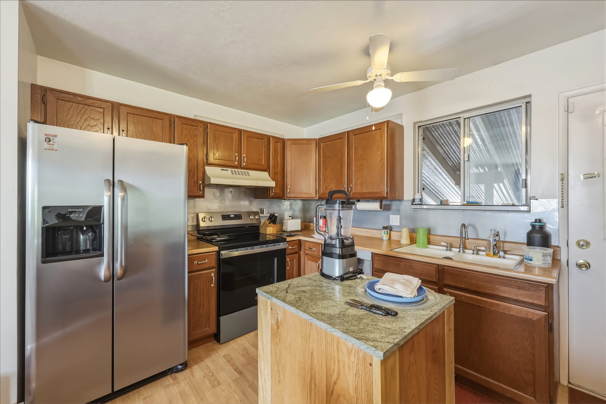 Kitchen featuring wood cabinetry, stainless steel appliances, a center island with a stone-finish countertop, and wood-finish flooring