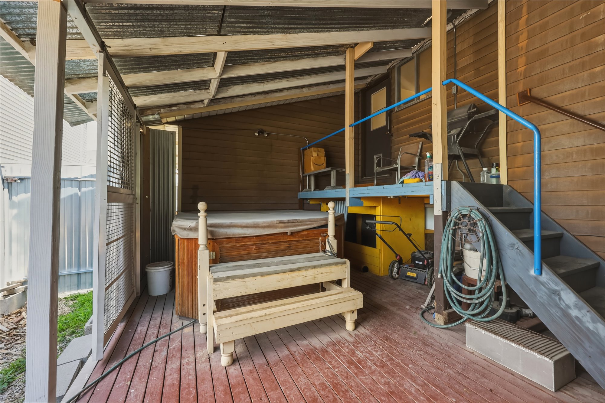 Covered outdoor deck area featuring a built-in spa, red-finish wood decking, and a corrugated metal roof